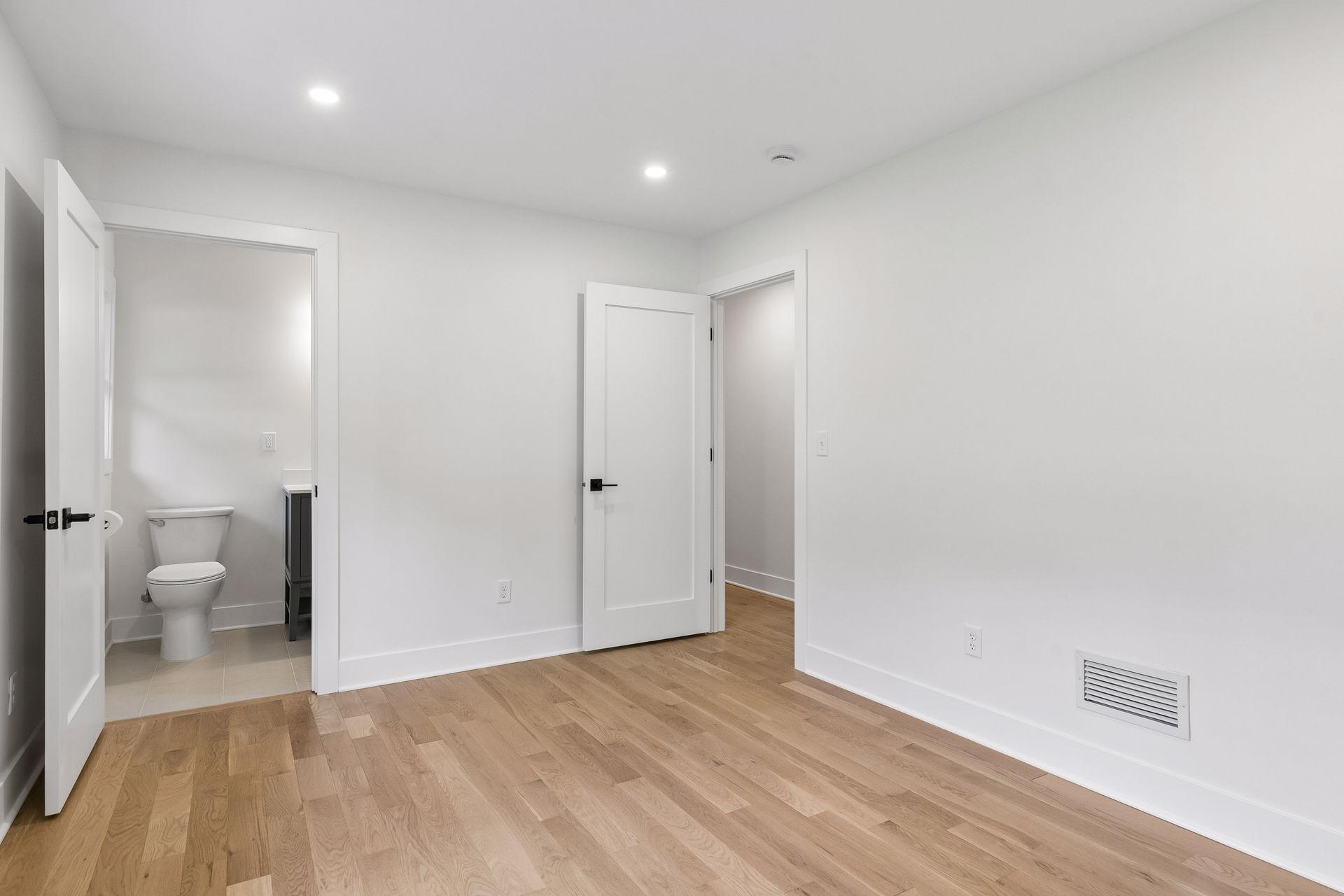 Empty room with light wood floors, an open bathroom doorway, and a second doorway.