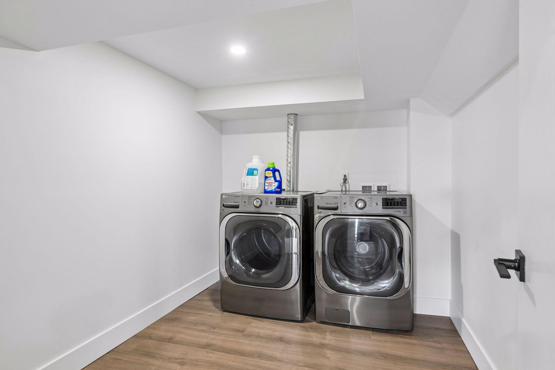 Laundry room with side-by-side stainless front-loading washer and dryer.