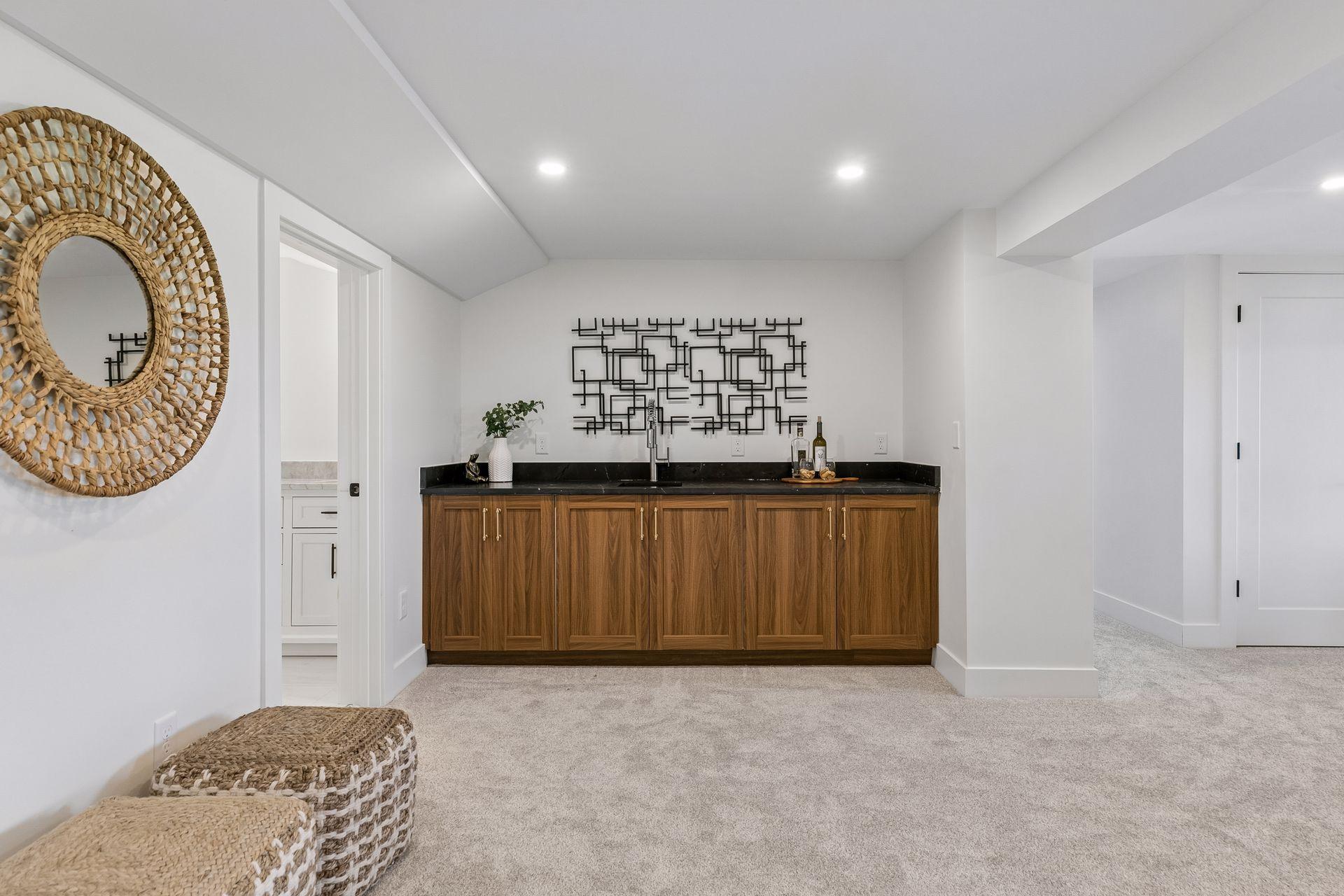 Basement wet bar with walnut cabinets, black countertop, sink, and geometric wall art.