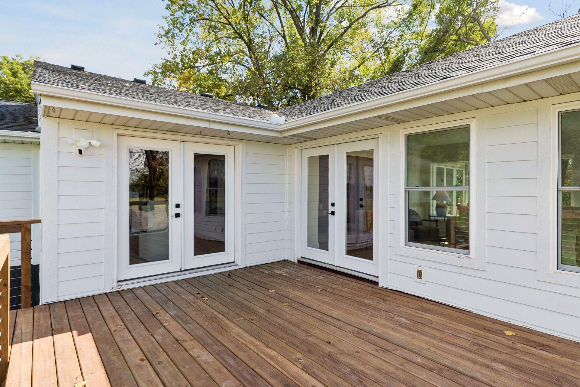 Wooden deck beside white siding, with several glass doors and windows opening onto it.