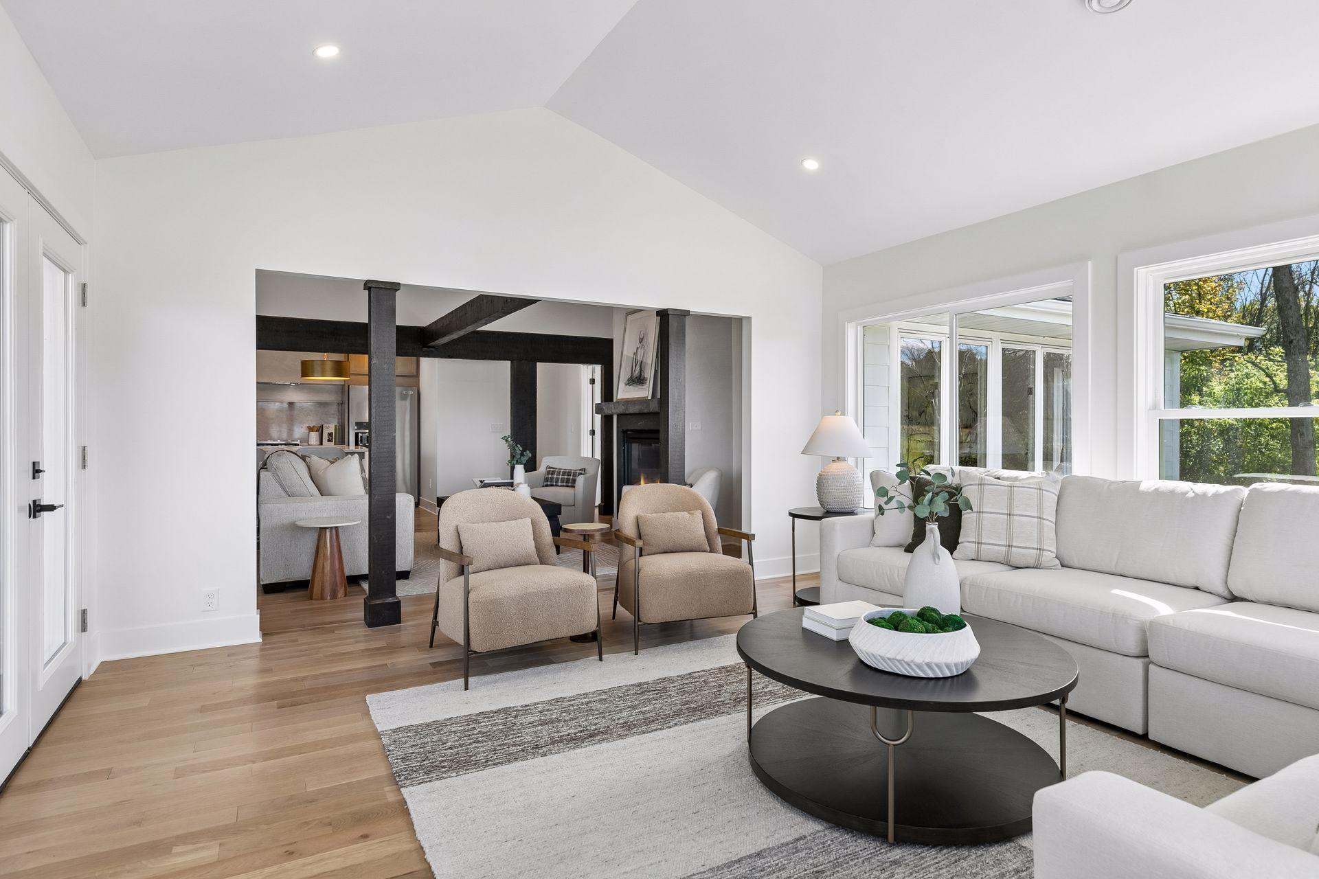 Staged living room with vaulted ceiling, dark exposed beams, fireplace, and large windows.