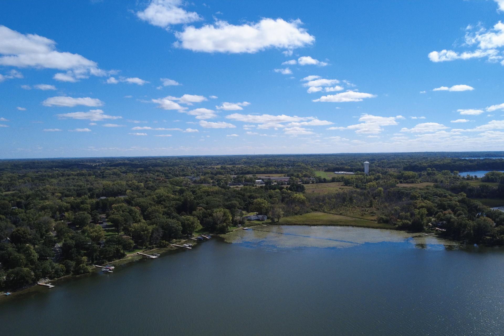 Aerial view of a wooded lakeshore neighborhood with docks and open water.