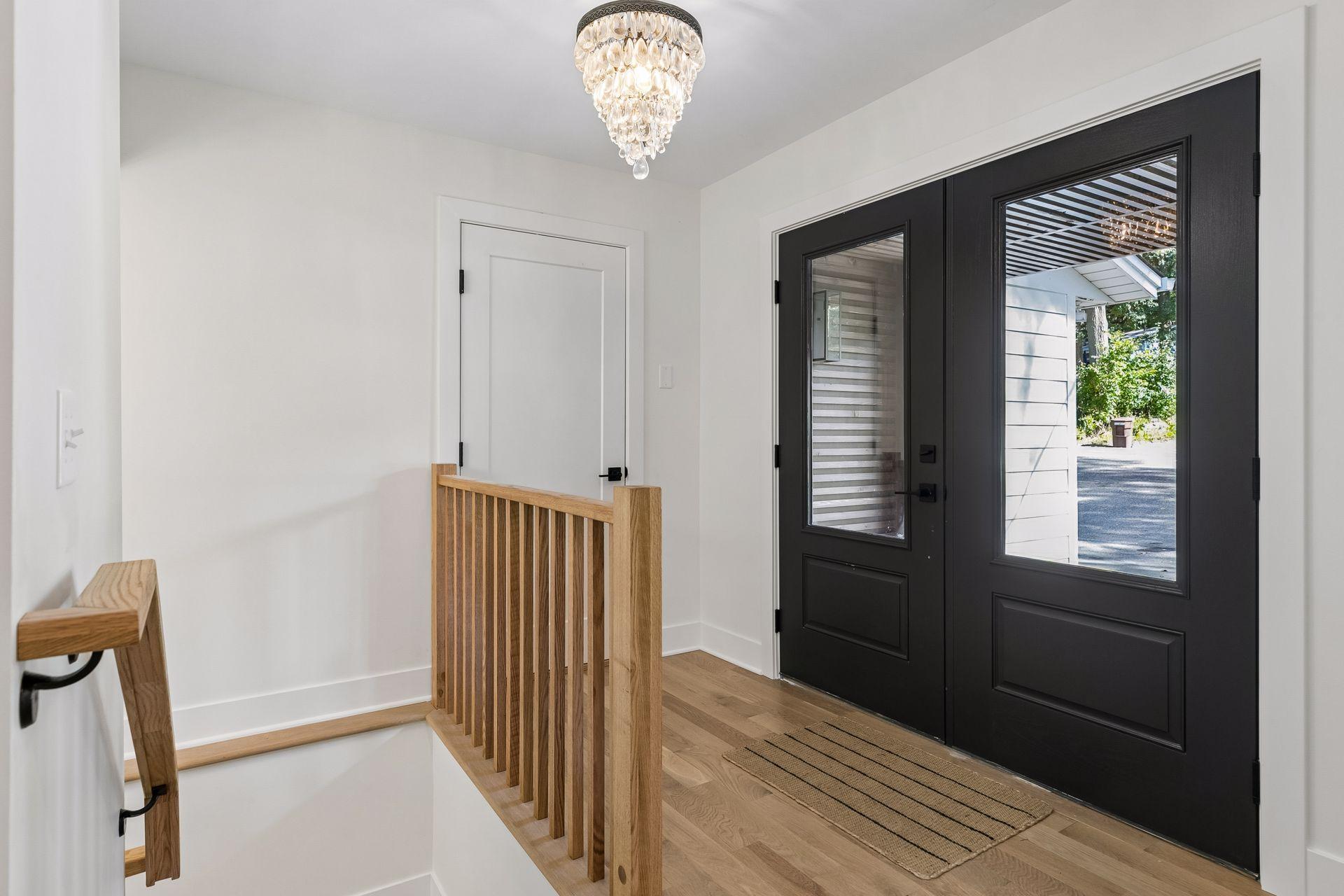 Entry foyer with black double doors, a wood staircase railing, and a crystal chandelier.