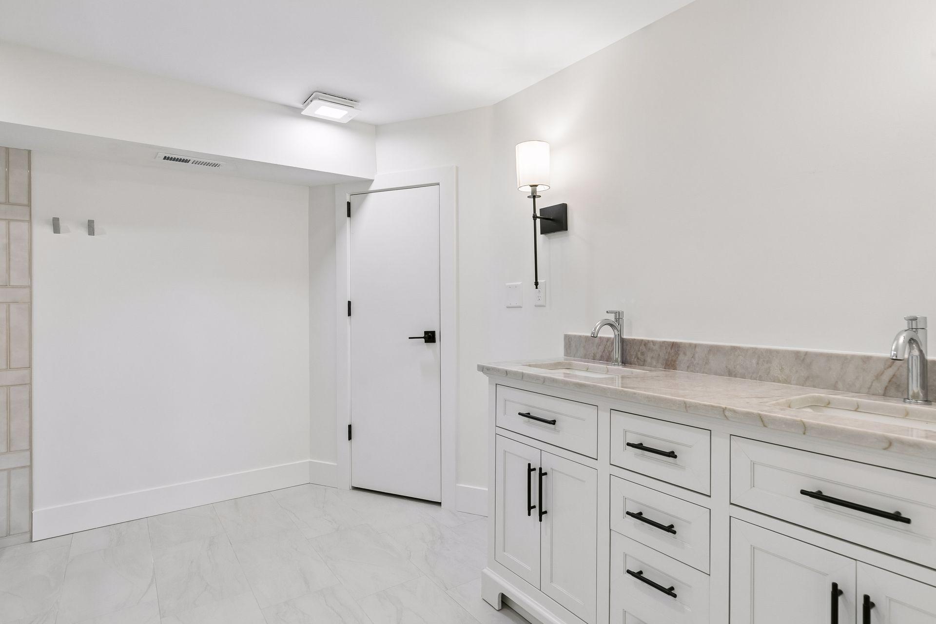 Bright bathroom with a double-sink vanity, marble-look counter, and white cabinetry with black hardware.