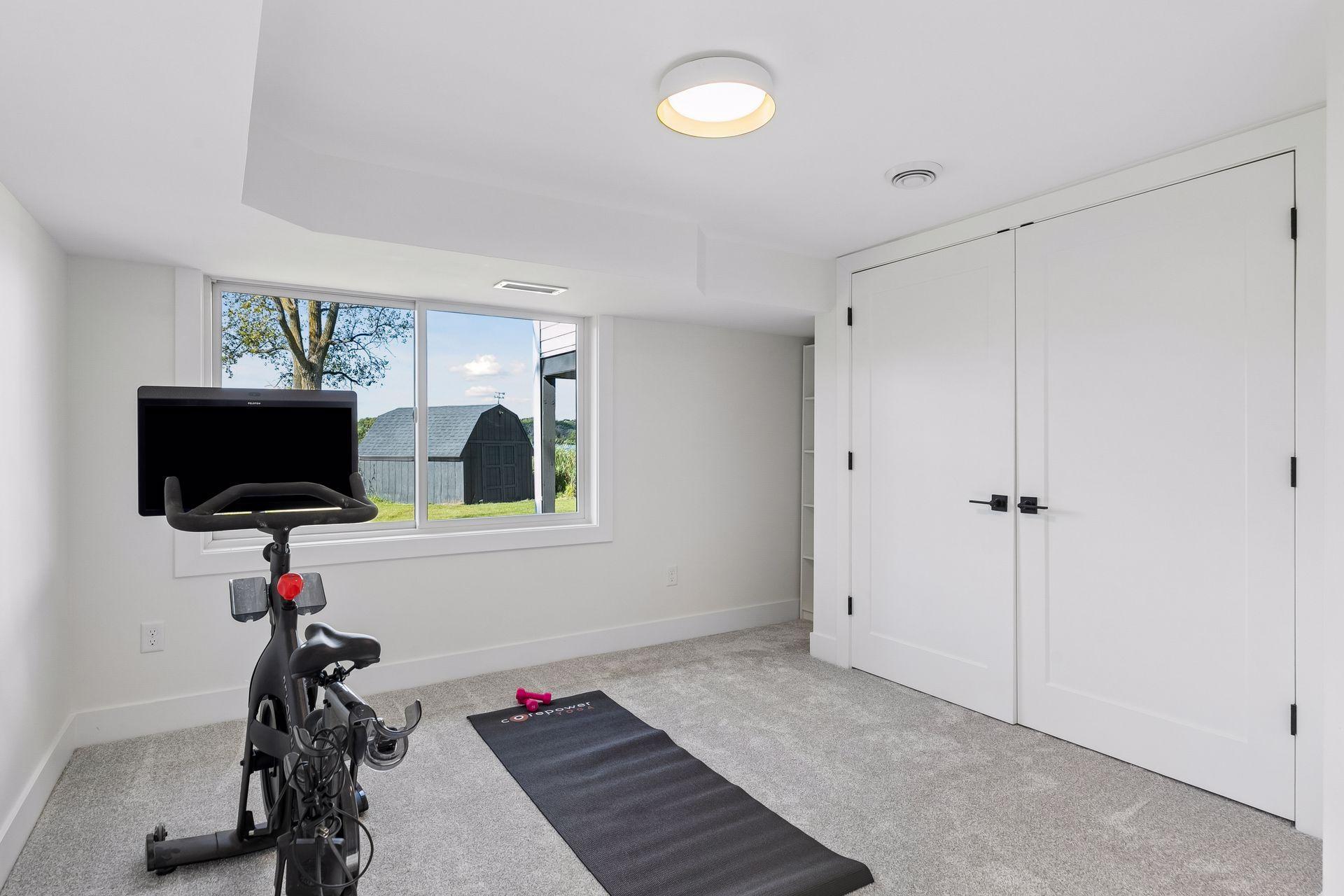 Exercise room with a stationary bike and mat beside a wide window and large double doors.