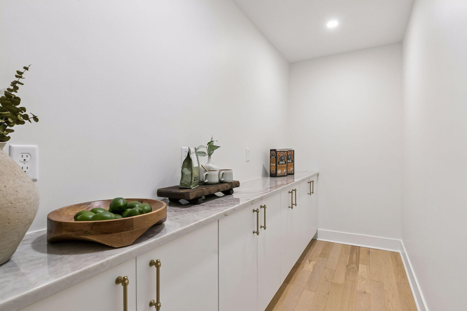 White built-in cabinets with brass pulls and a long marble-look counter, styled with fruit and cups.