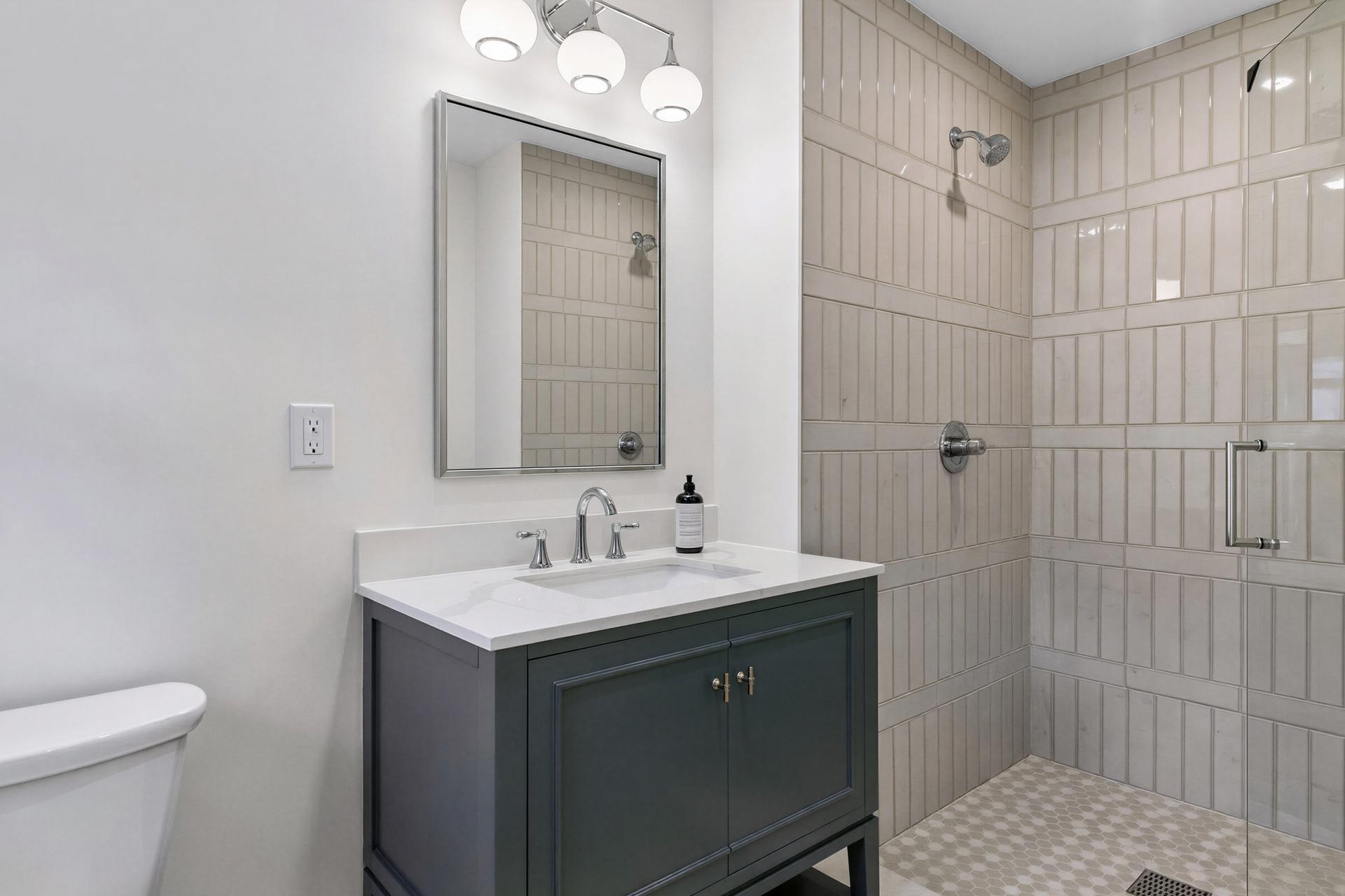 Bathroom with a dark green vanity, framed mirror, and tiled walk-in shower.
