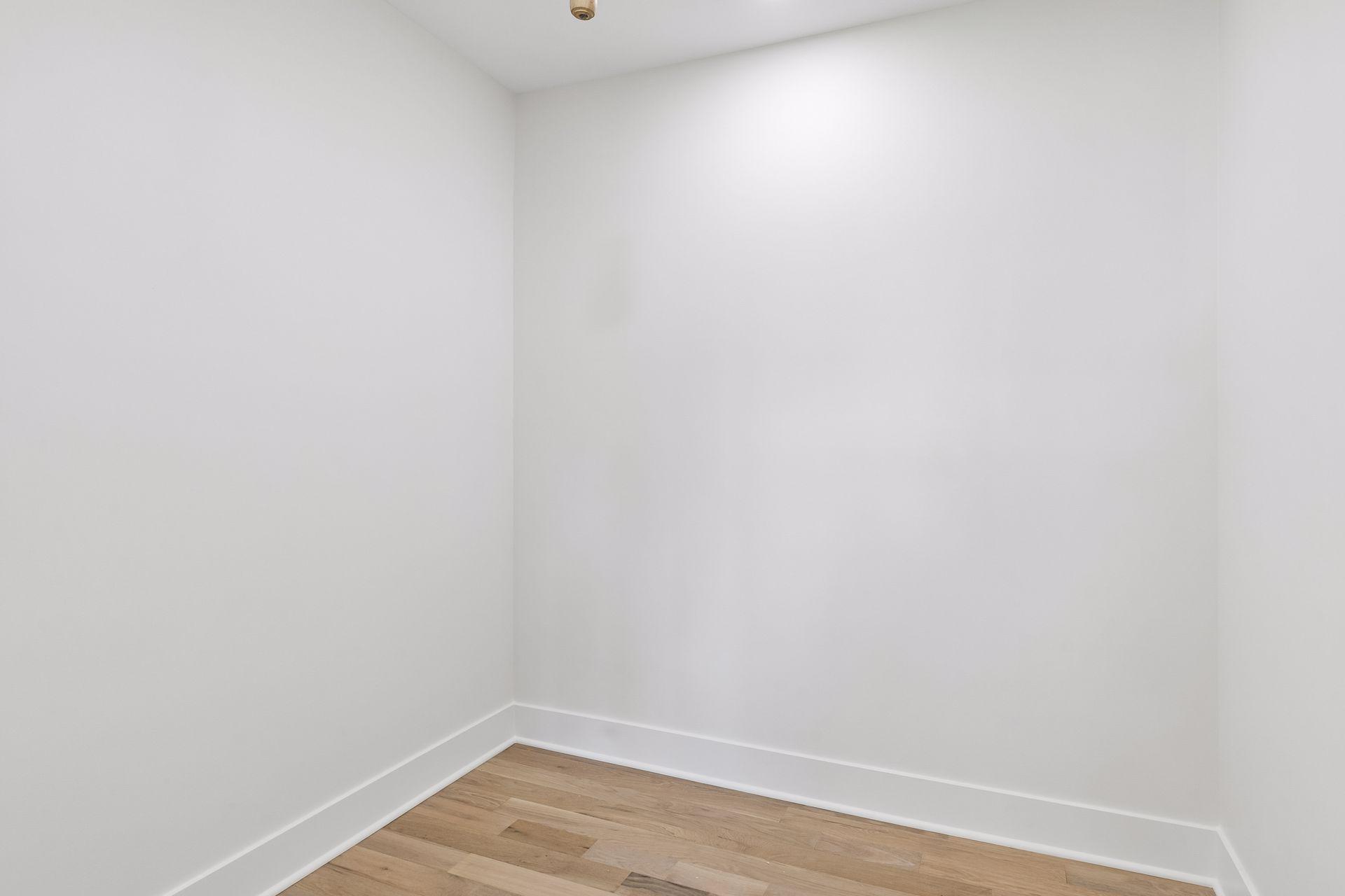Empty room corner with white walls and light wood plank flooring.
