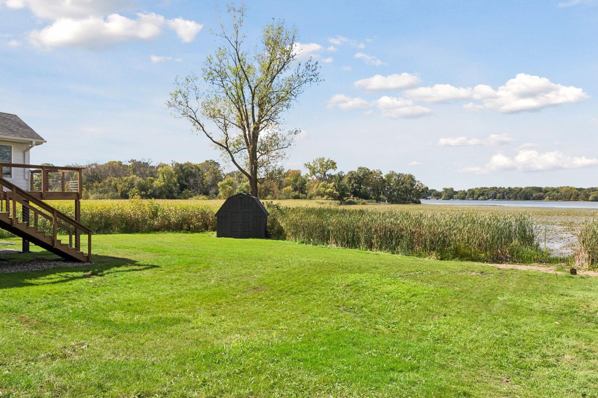 Waterfront lawn with a small shed, deck stairs, and lake bordered by reeds.