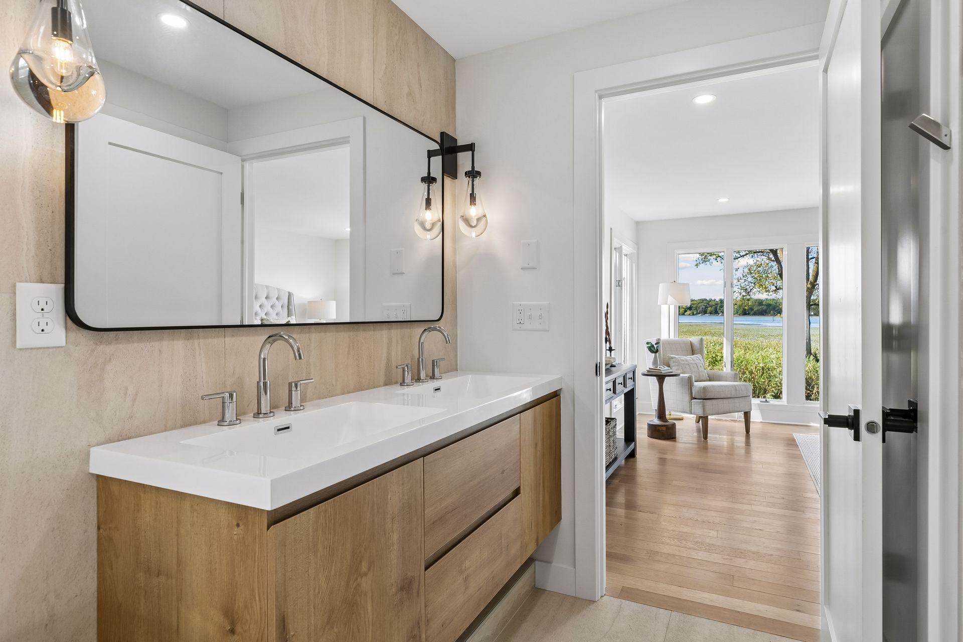 Bathroom with a double-sink wood vanity and a view toward a lakefront sitting area.