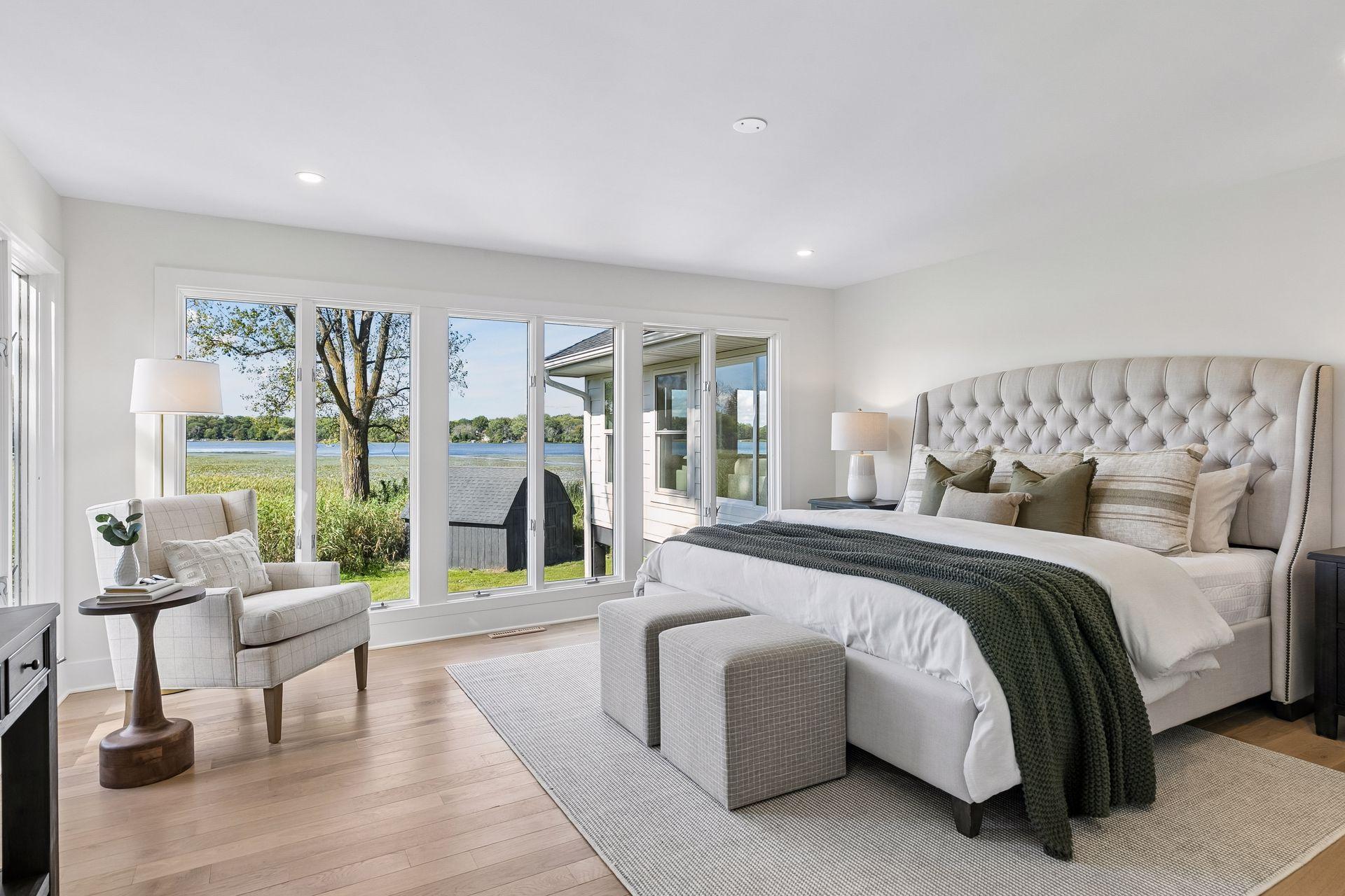 Staged bedroom with a tufted bed and wide windows overlooking the lake.