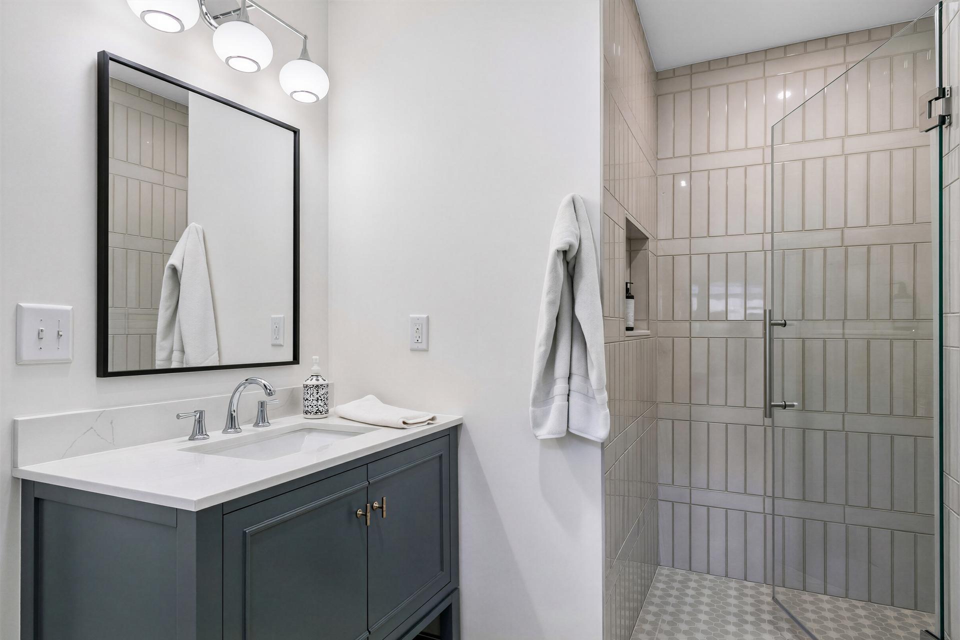 Bathroom with a dark blue vanity and a glass-enclosed, tiled walk-in shower.