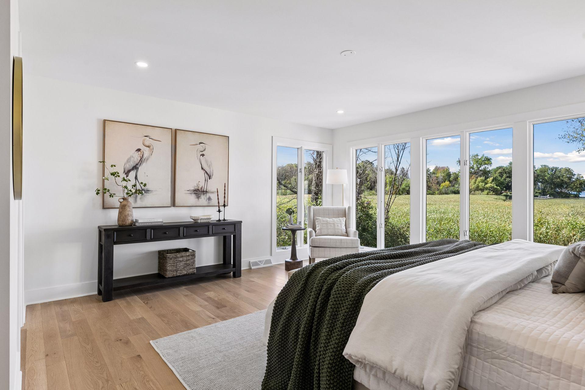 Staged bedroom with a dark green bed throw and tall windows overlooking a grassy field.