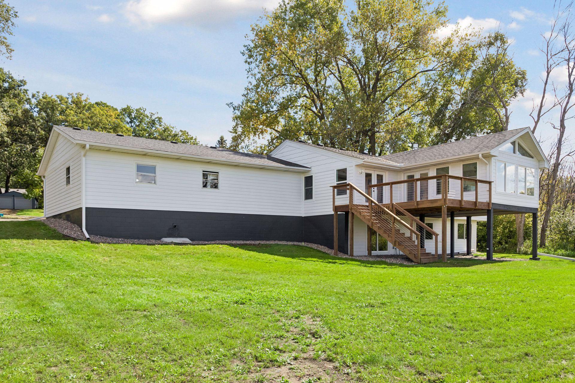 Rear exterior of a white home with a raised wooden deck and stairs across a green lawn.