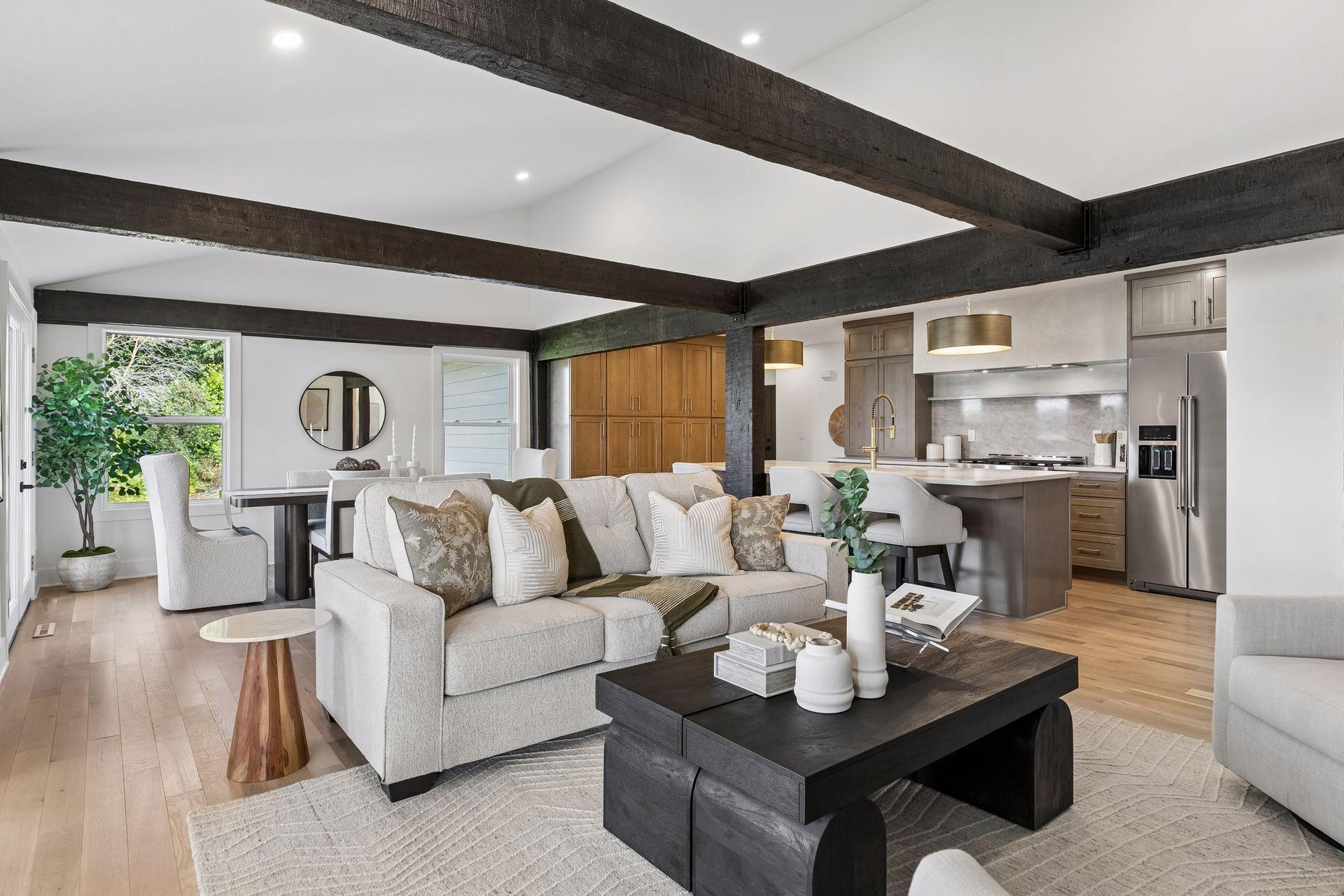 Open living room and kitchen with exposed dark beams, light wood floors, and a large island.