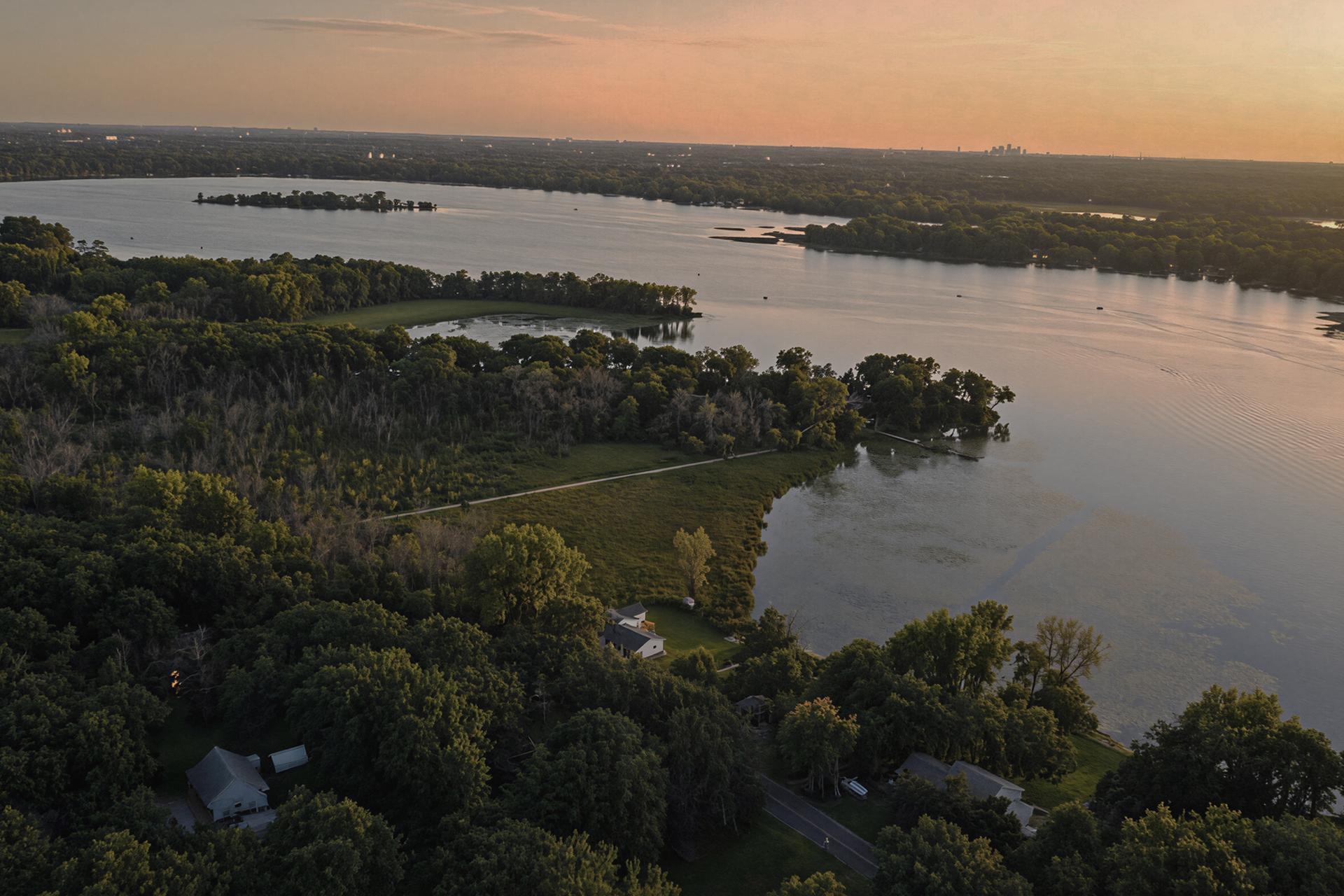Bald Eagle Lake at golden hour, with wooded islands and homes along its shoreline.