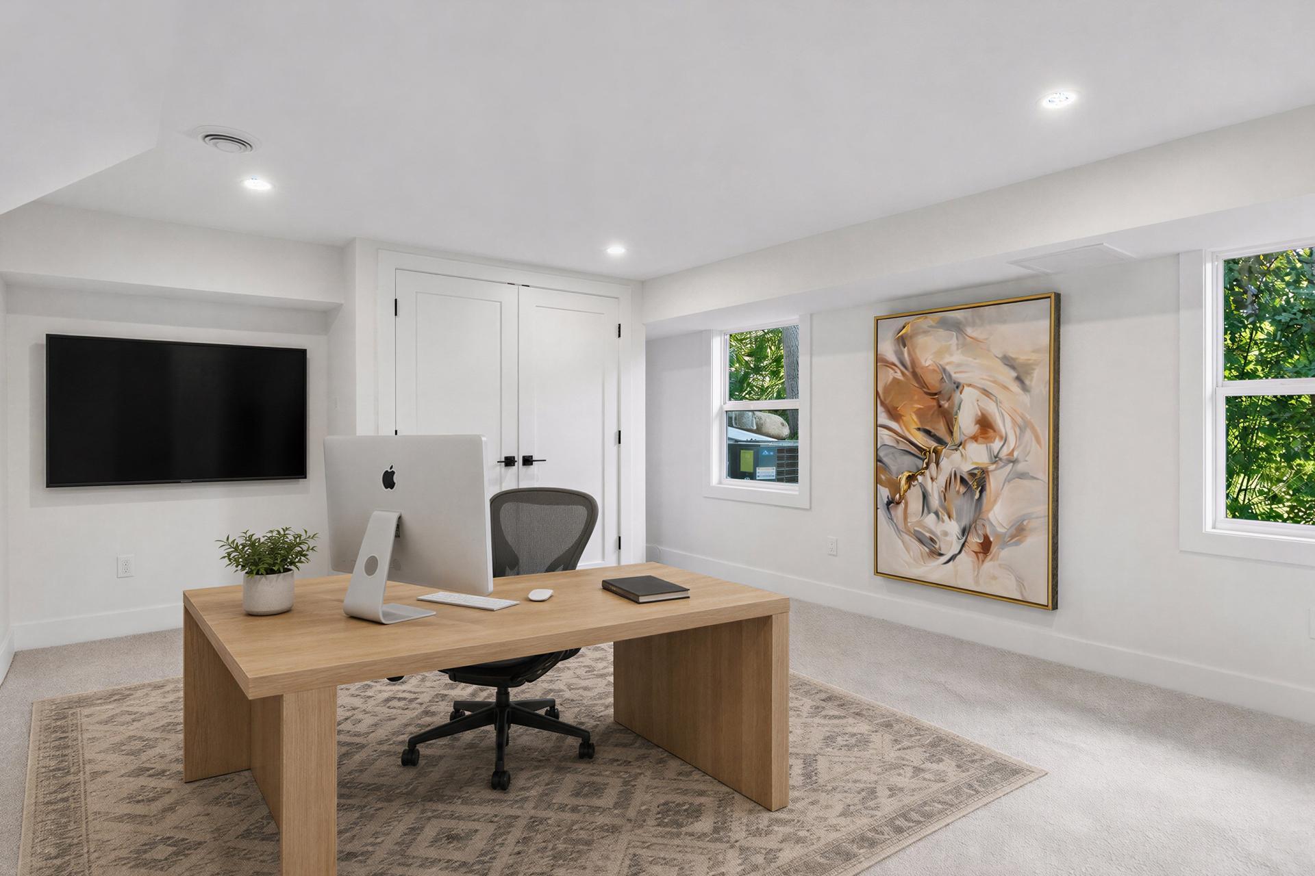 Furnished home office with a wooden desk, wall-mounted television, and framed abstract artwork.