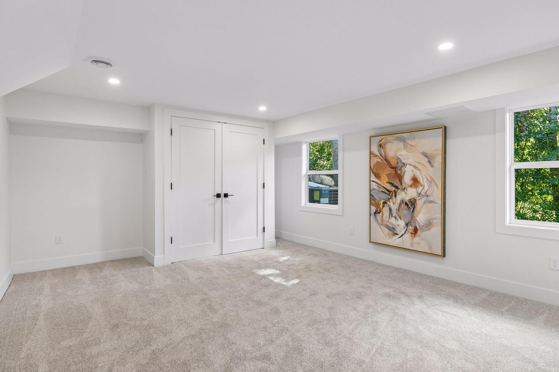 Carpeted room with double closet doors, two windows, and a large abstract painting.