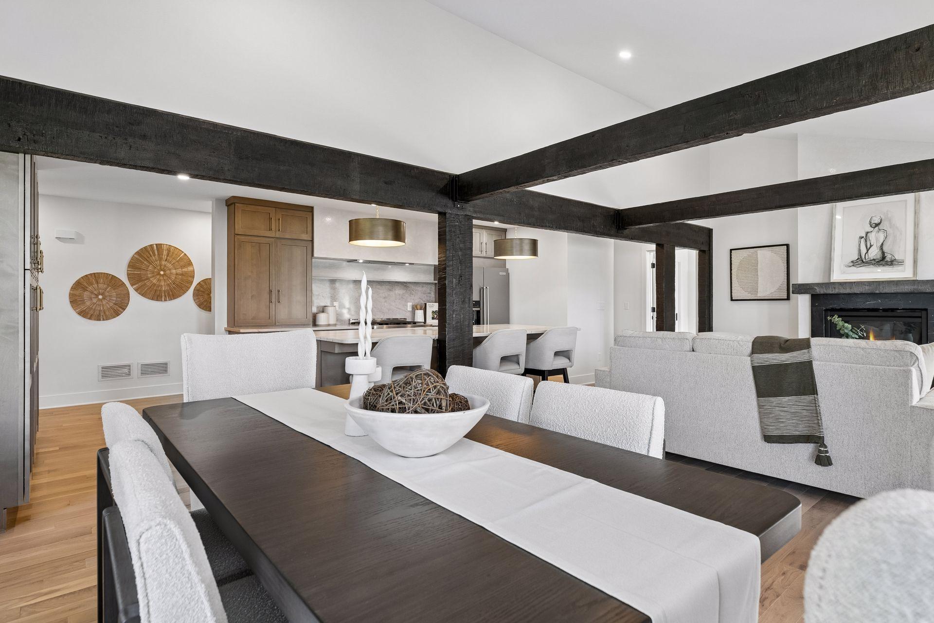 Open-concept dining and living room with exposed dark beams, a kitchen island, and fireplace.