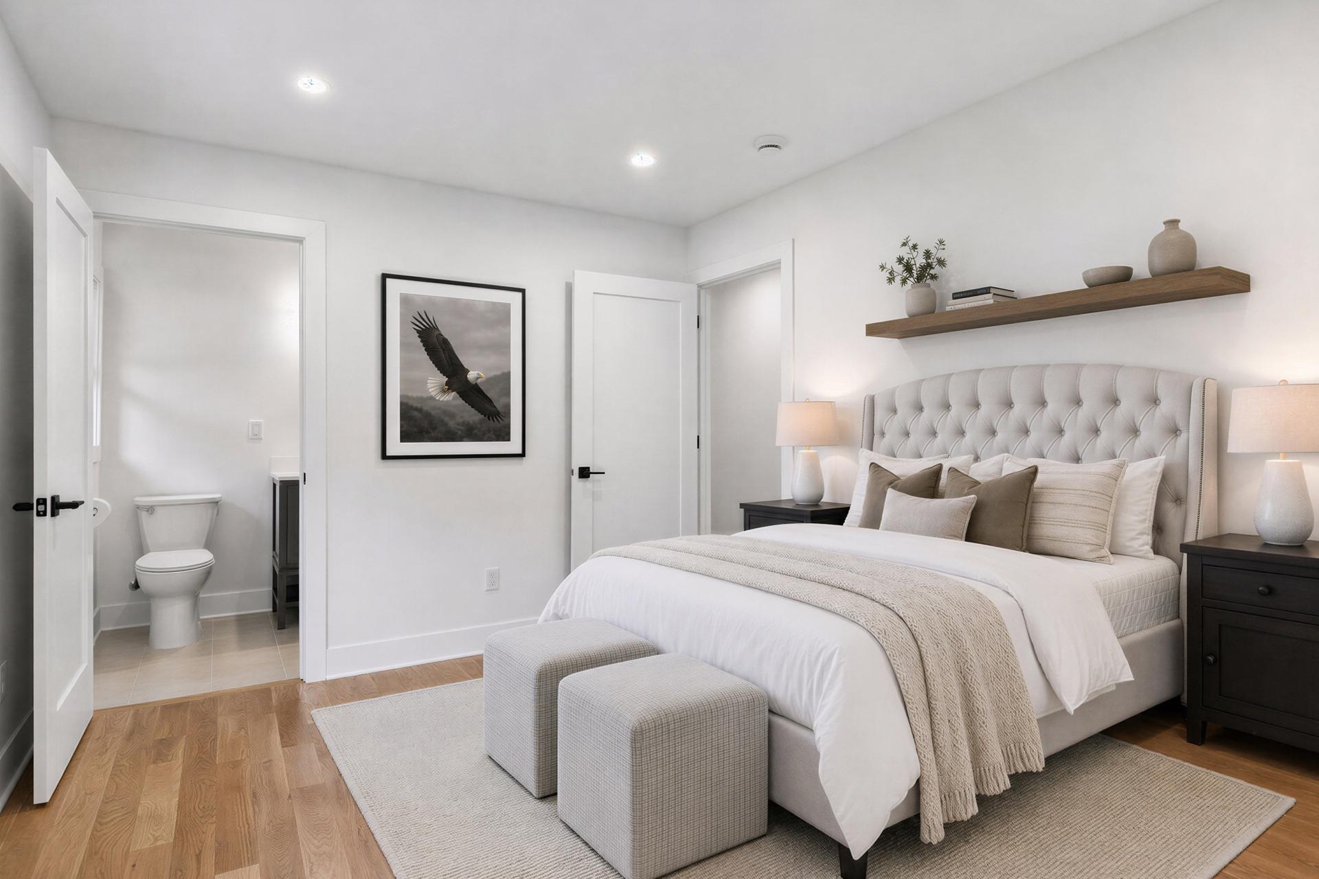 Staged bedroom with a tufted bed and neutral bedding, opening to an adjoining bathroom.