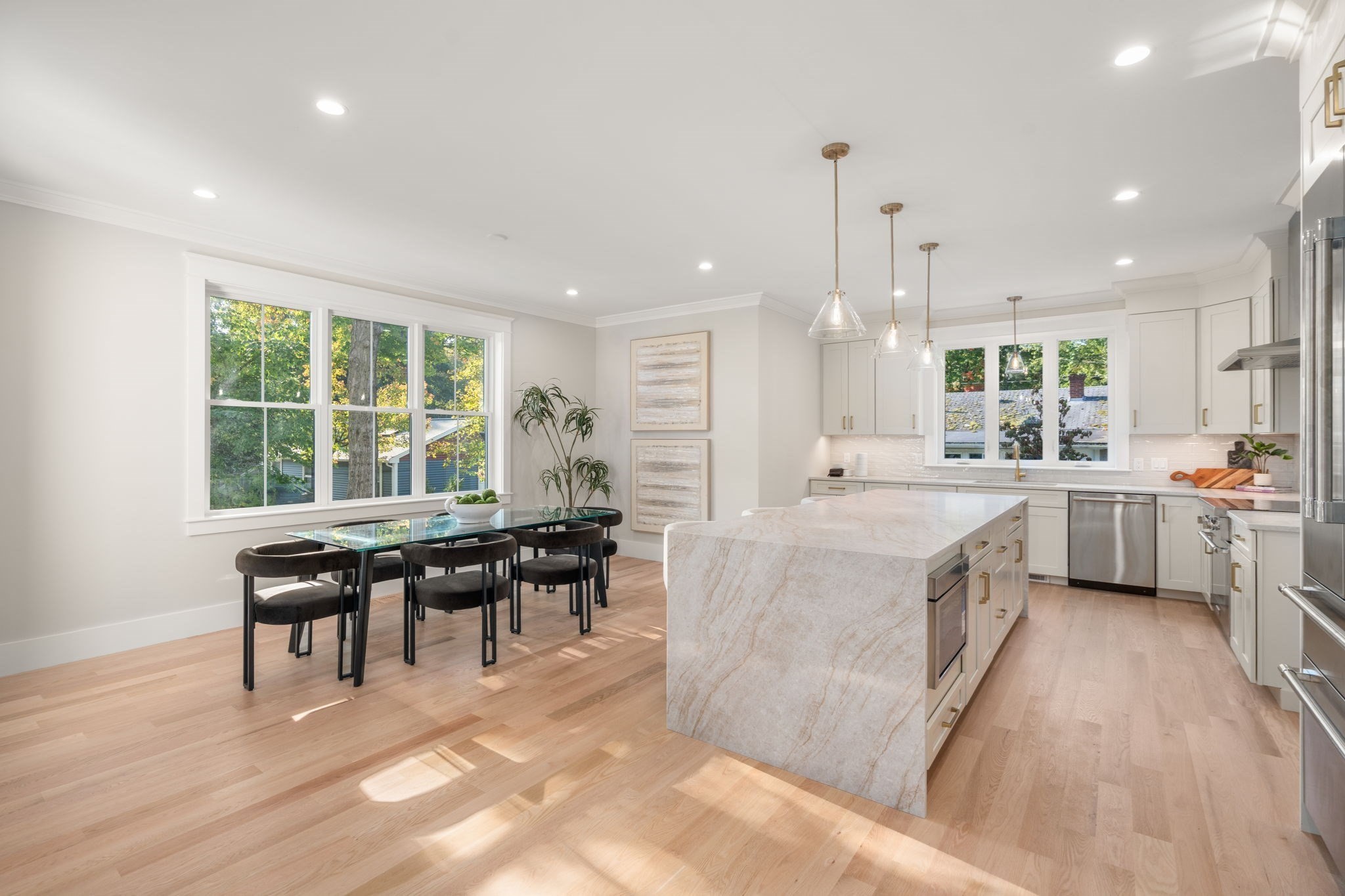 Open-plan kitchen with a large marble-patterned island and glass dining table beside wide windows.