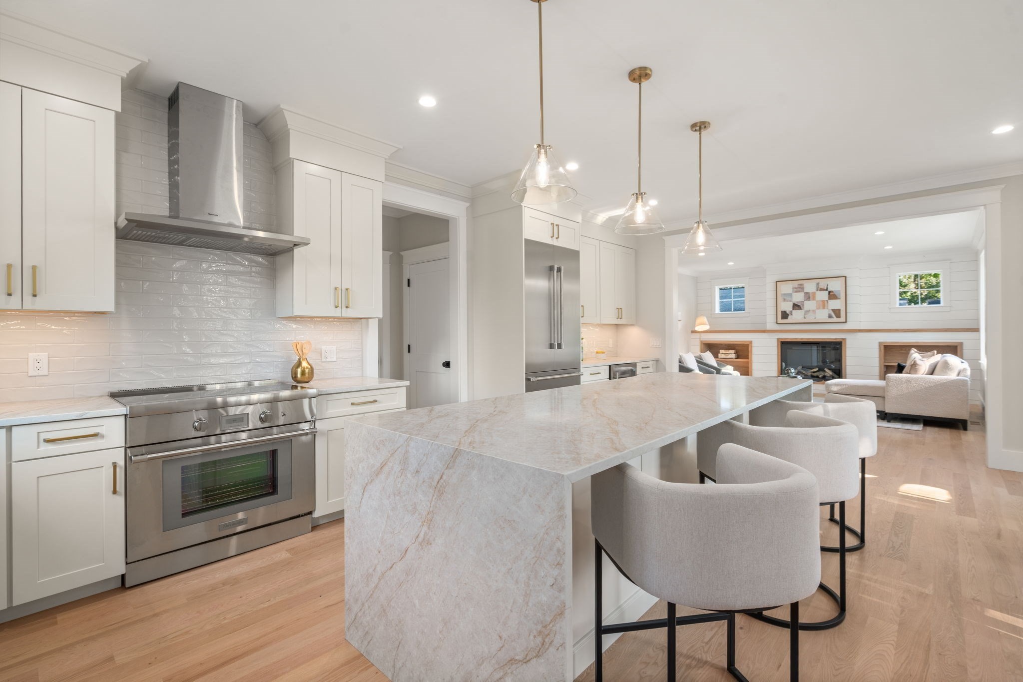 Bright kitchen with a marble waterfall island, bar seating, and an adjoining living room with a fireplace.