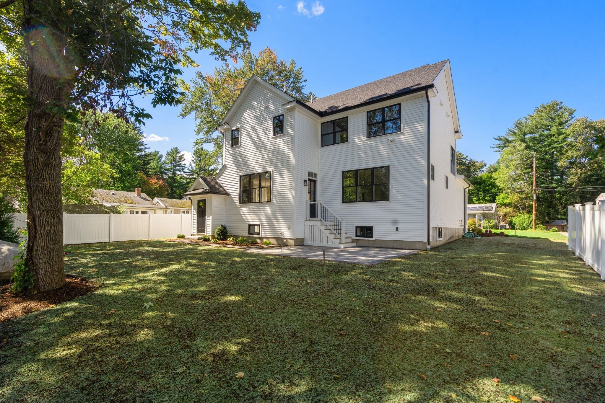 White two-story house viewed from the backyard, with dark-framed windows and a broad lawn.