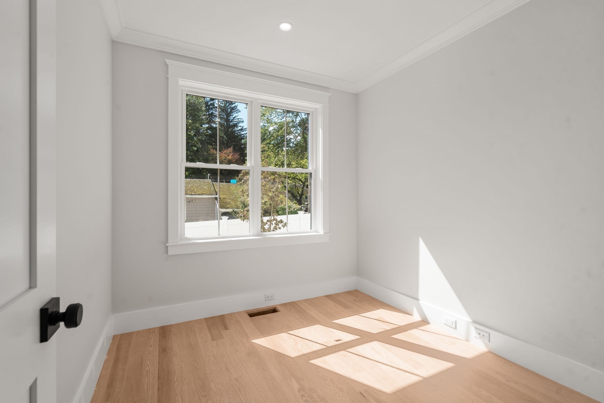 Empty room with light oak floors and a large window overlooking trees.