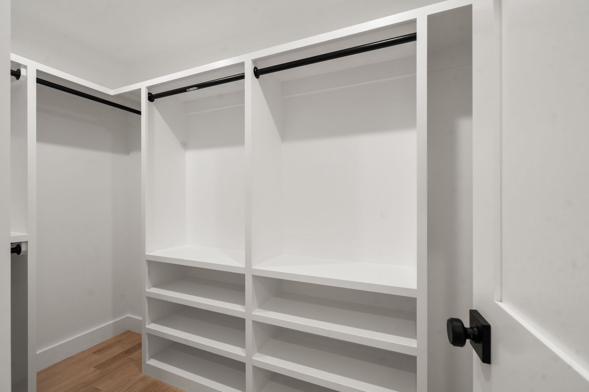 Walk-in closet with white built-in shelves, black hanging rods, and wood flooring.