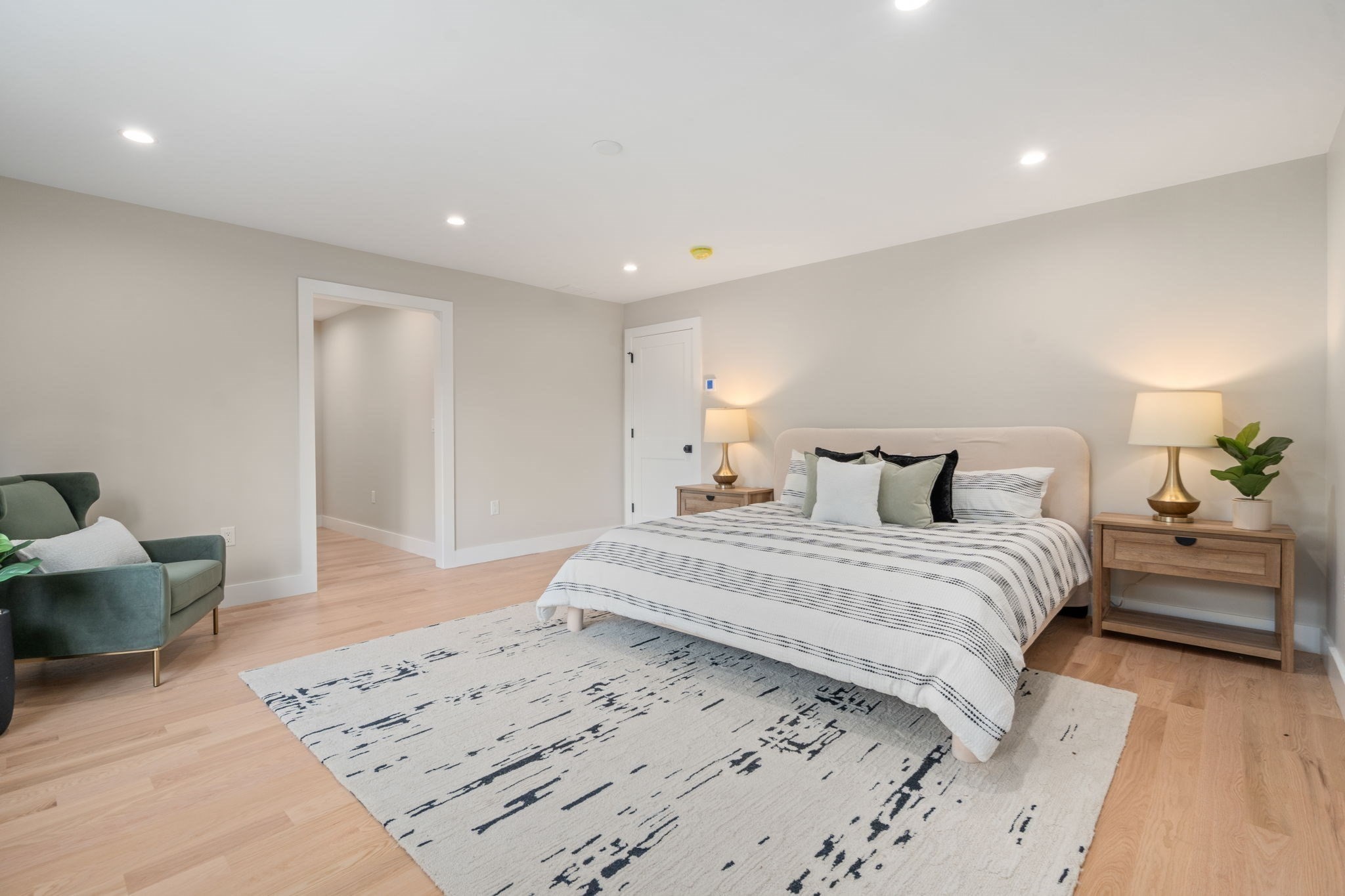 Staged bedroom with striped bedding, a large patterned rug, and a green armchair.