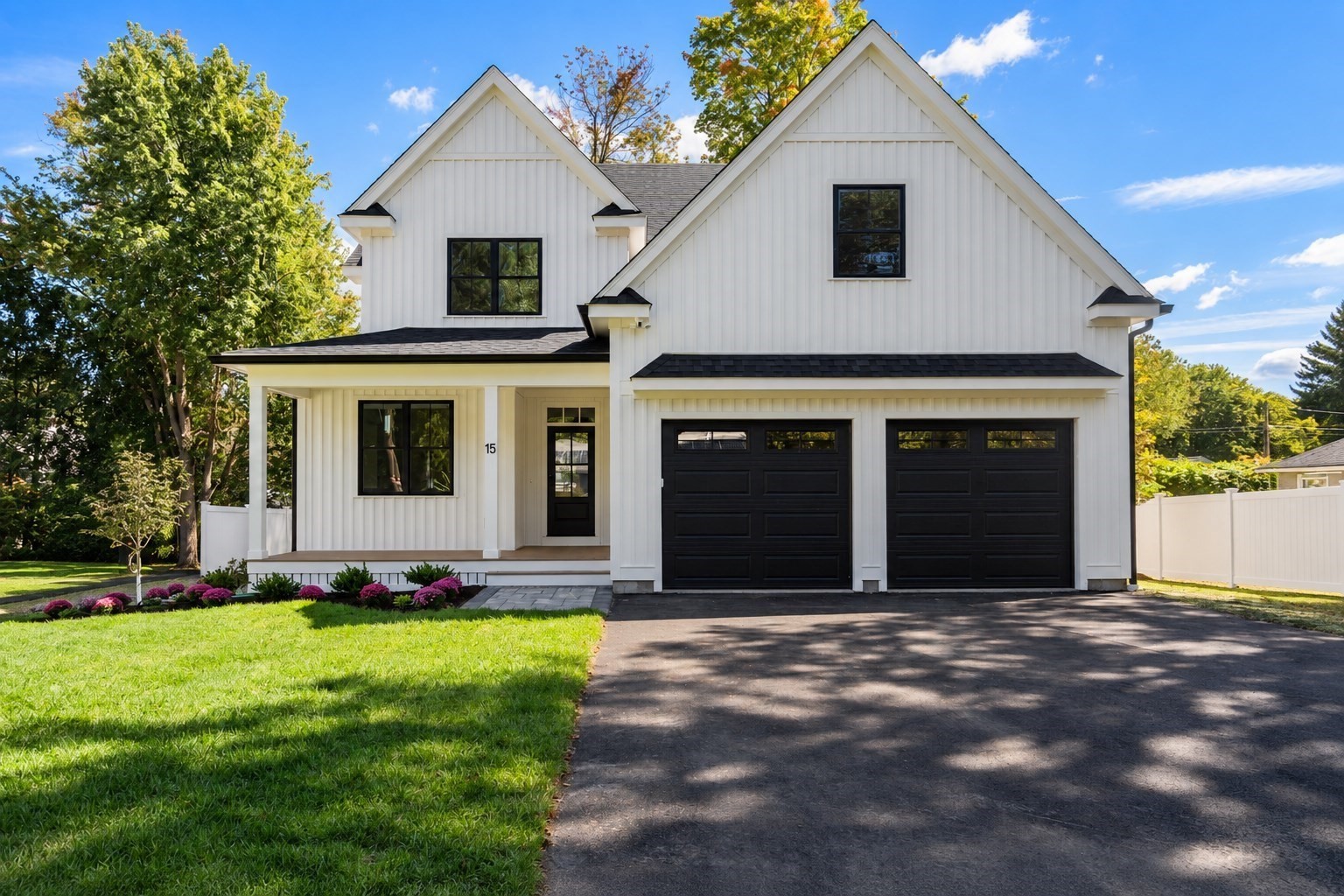 White two-story farmhouse with black double garage doors, covered porch, and landscaped front lawn.