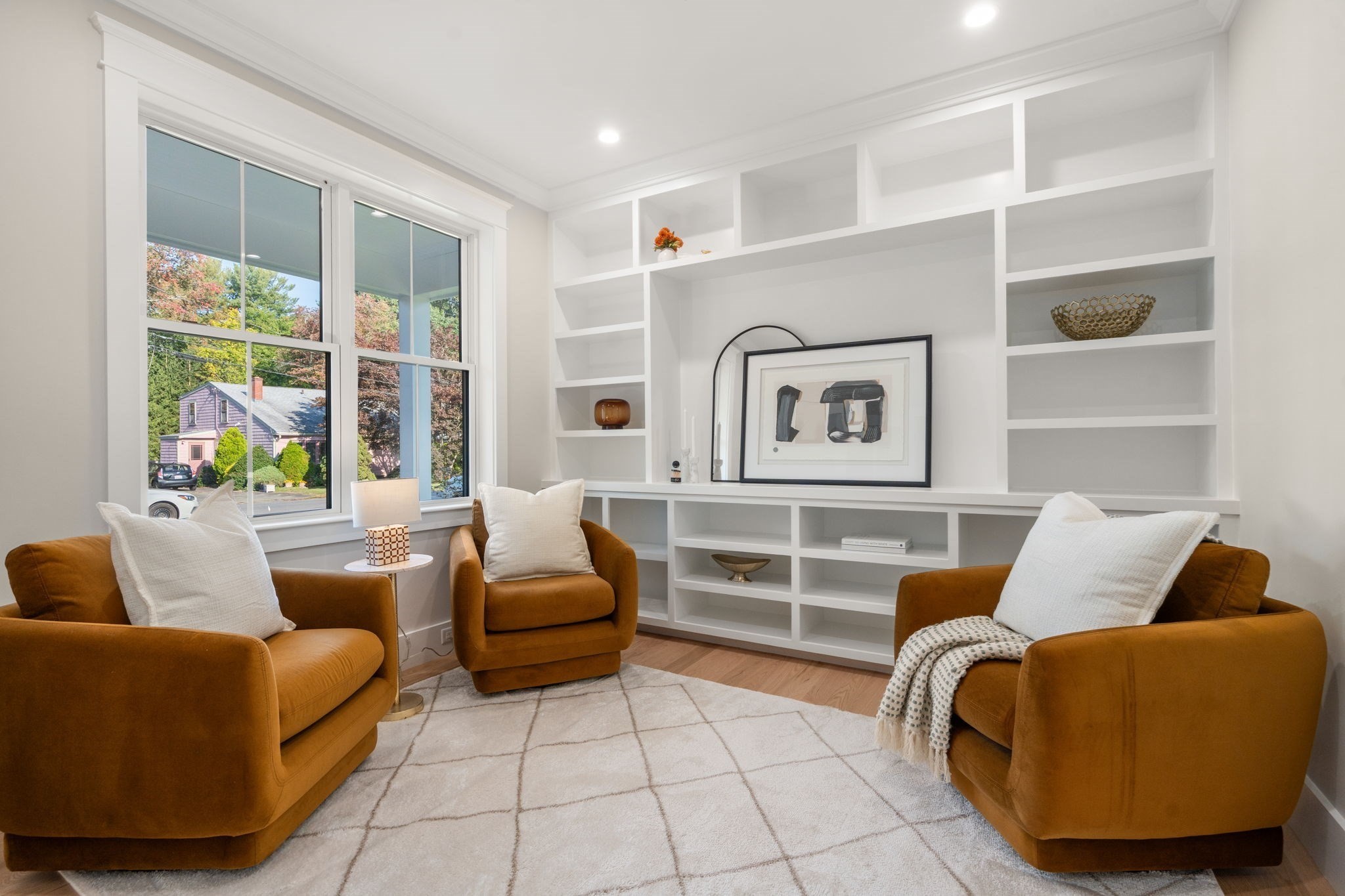 Sitting room with mustard armchairs, white built-in shelves, and large windows overlooking autumn trees.