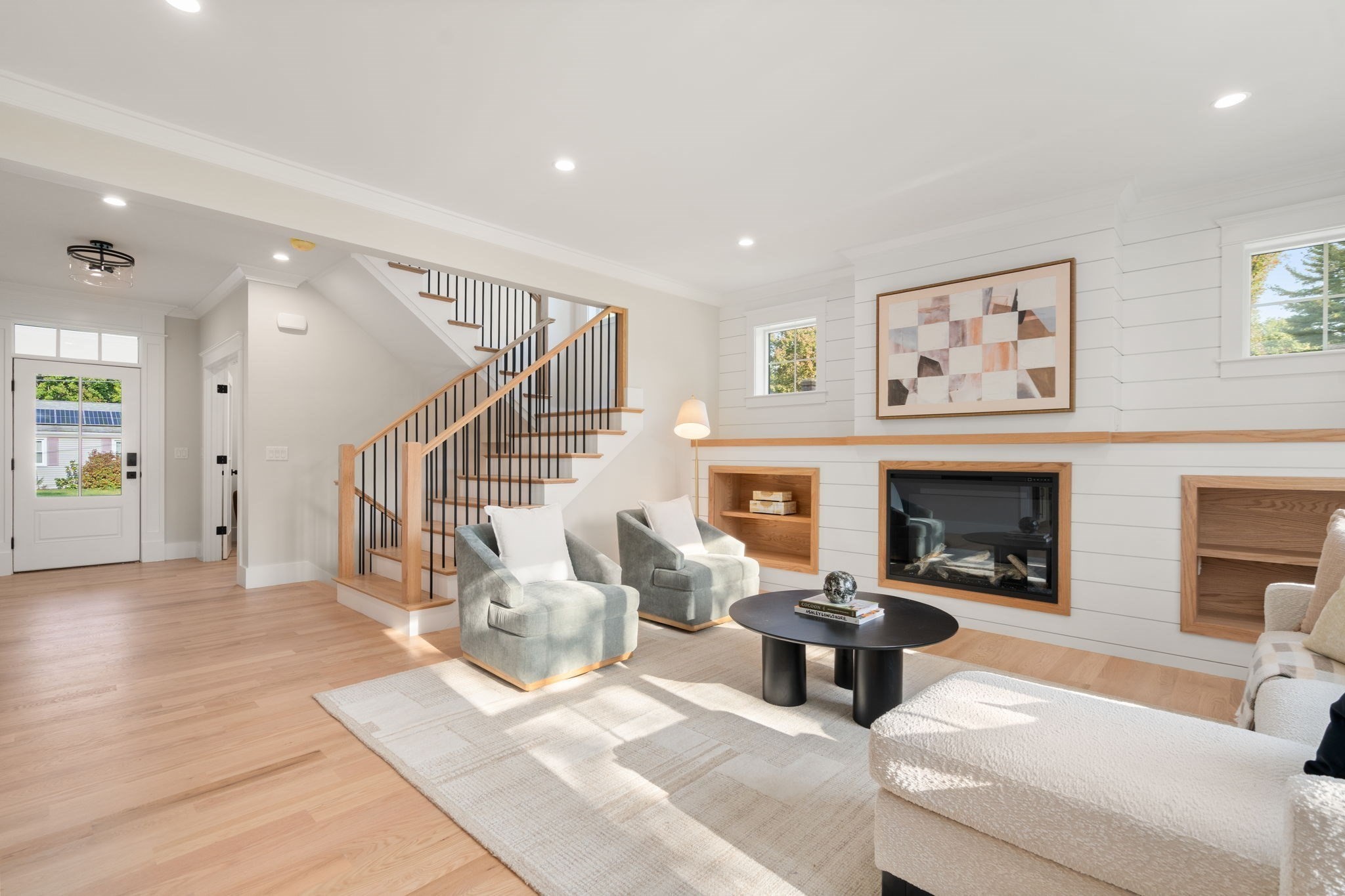 Staged living room with a white shiplap fireplace, built-in shelves, and a wood-and-black staircase.