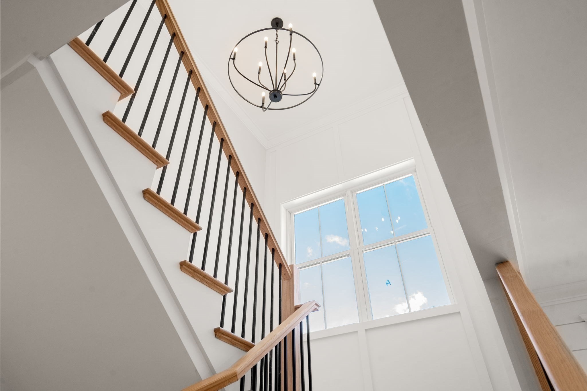 Entry foyer with a wood staircase, black balusters, tall window, and circular chandelier.