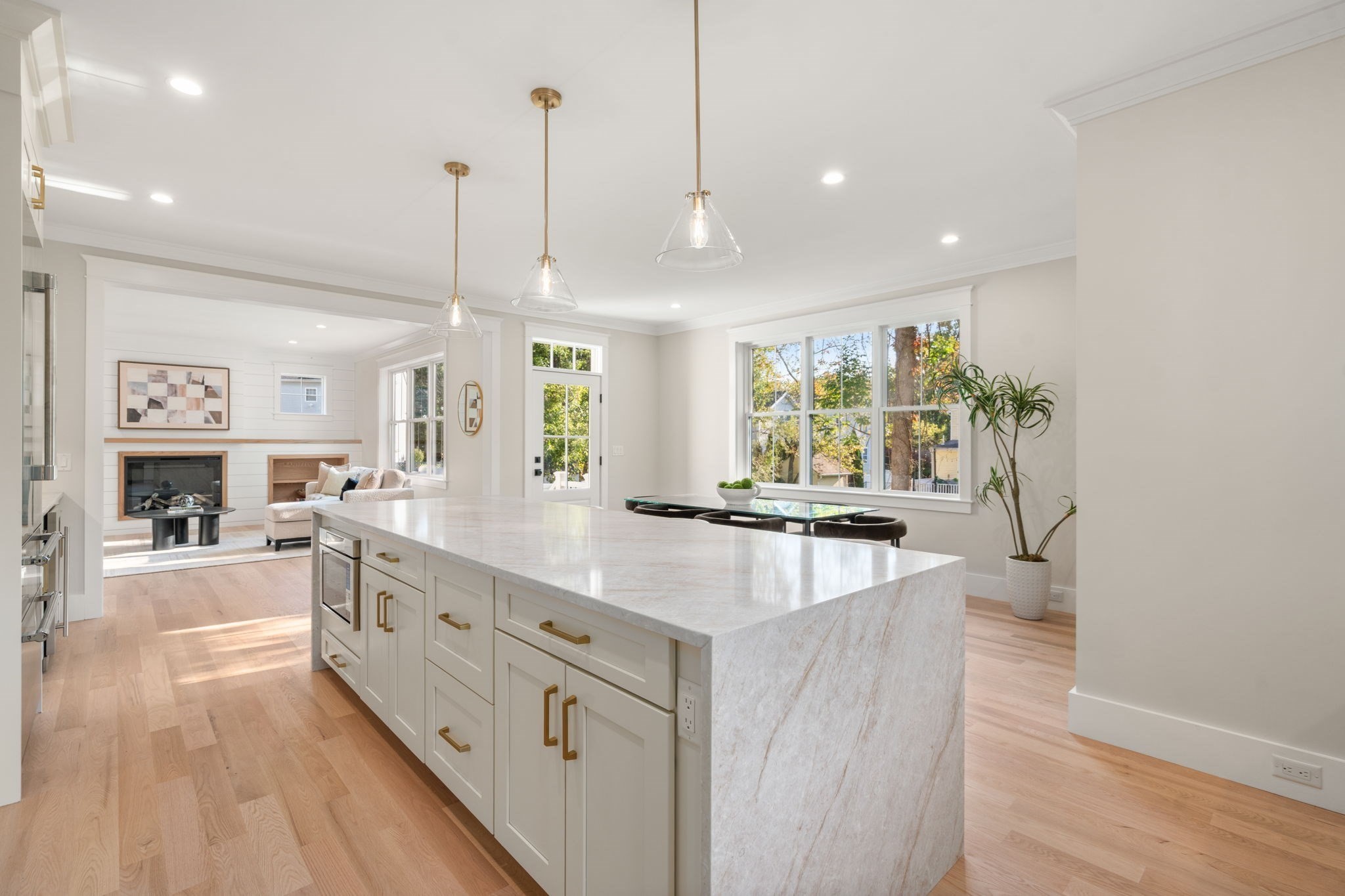 Open-plan kitchen with a large stone island, bright windows, and an adjoining living room with fireplace.