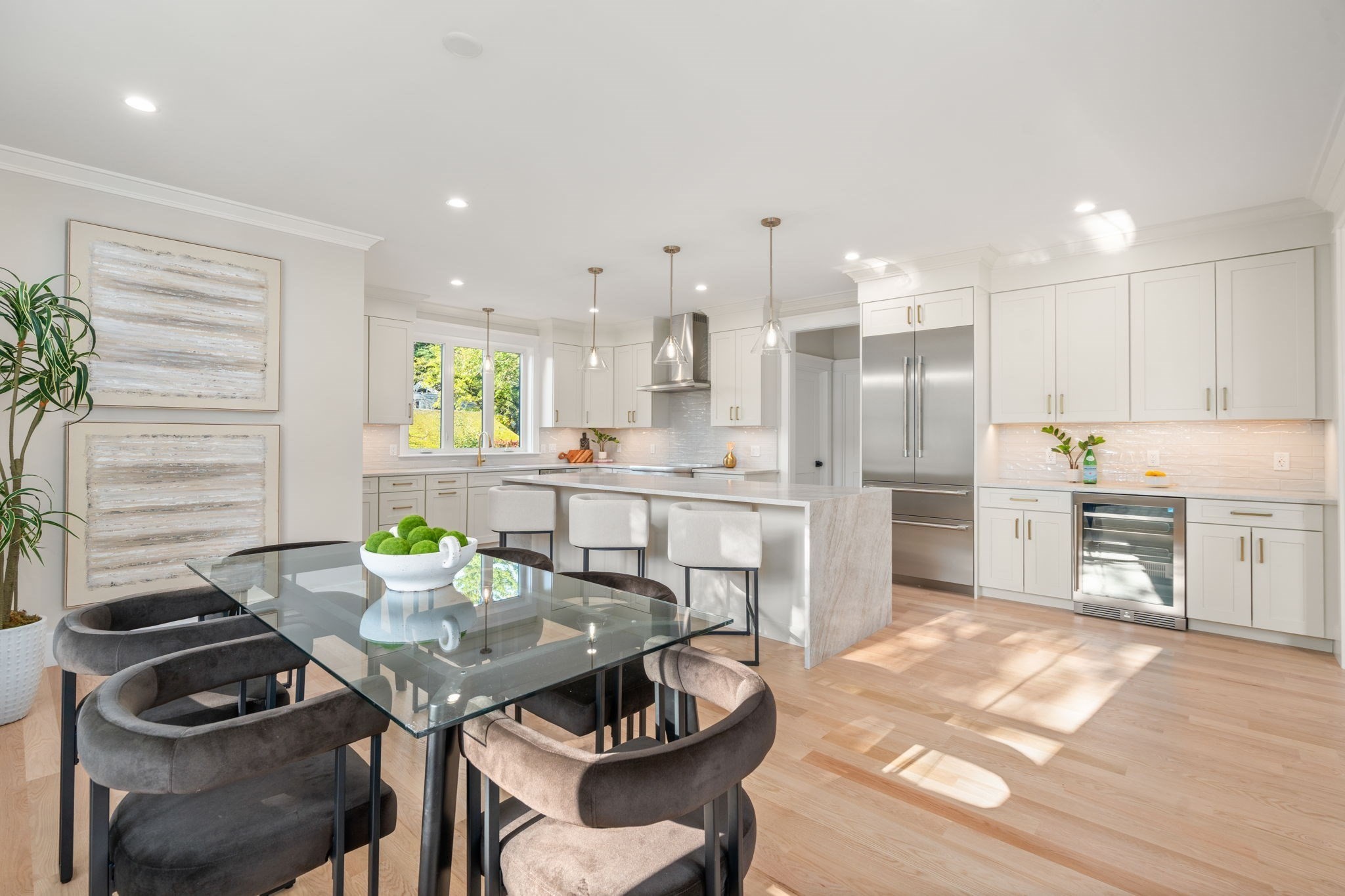 Bright white kitchen with a large island, stainless appliances, and an adjoining glass dining table.