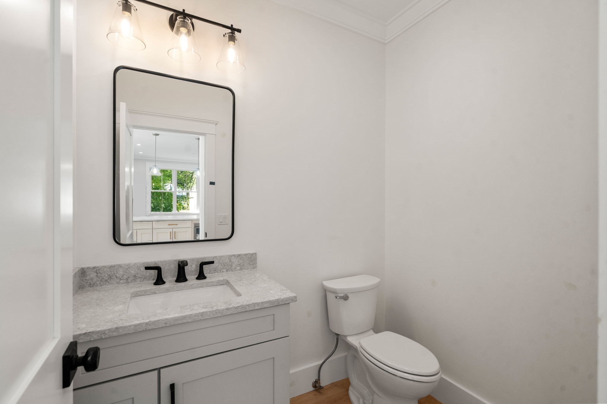 Bathroom with a gray vanity, marble-look counter, black fixtures, and a large mirror beside a white toilet.