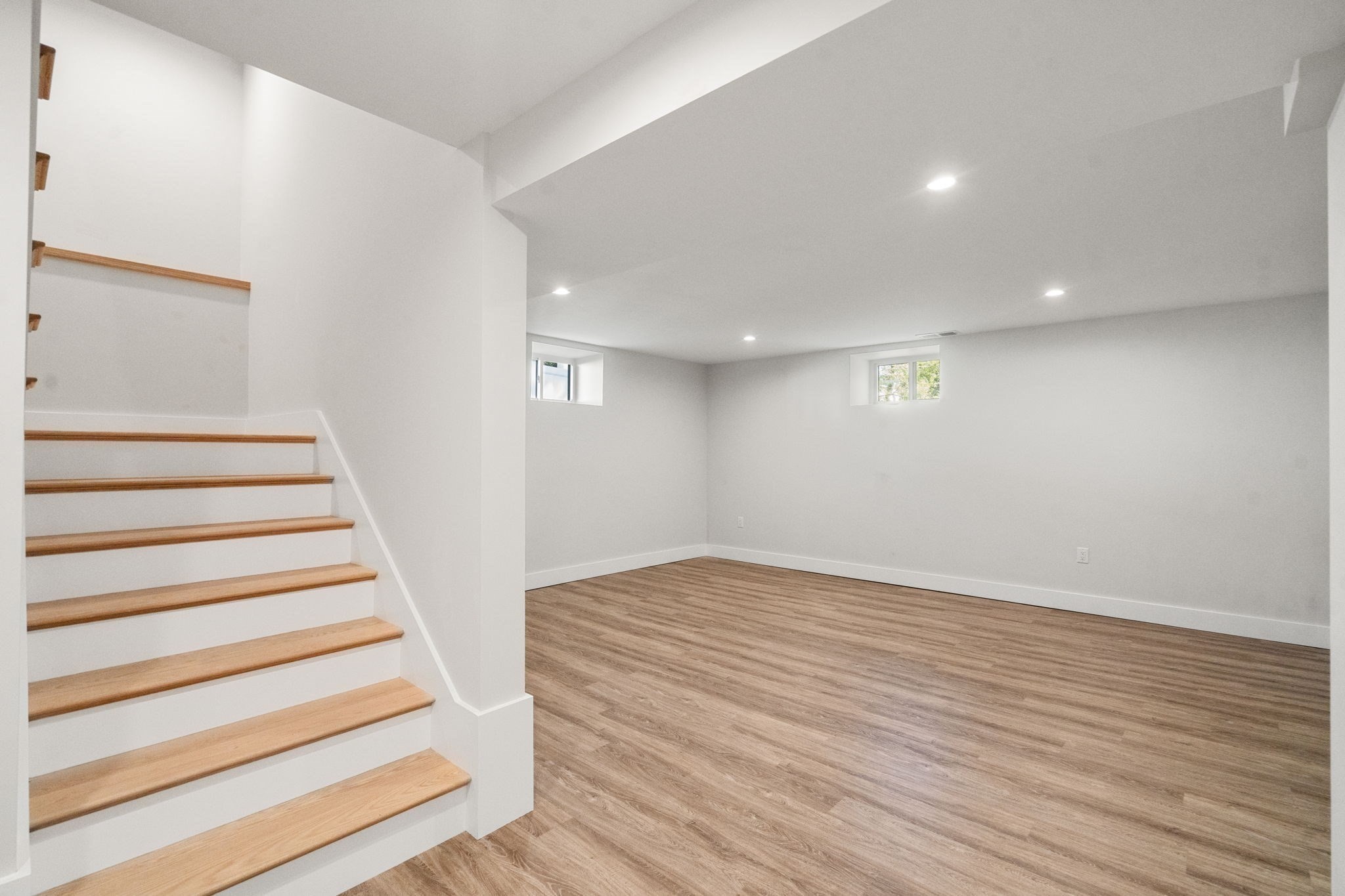 Unfurnished basement with wood-look flooring and a staircase with natural wood treads.