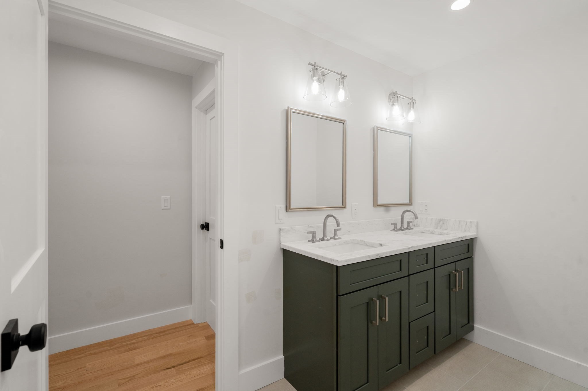Bathroom with a dark green double vanity, marble countertop, two sinks, and matching framed mirrors.