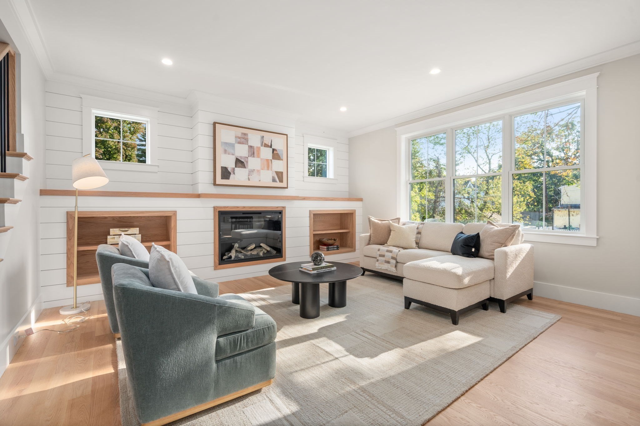 Living room with a shiplap fireplace, built-in shelves, and seating beside a large window.