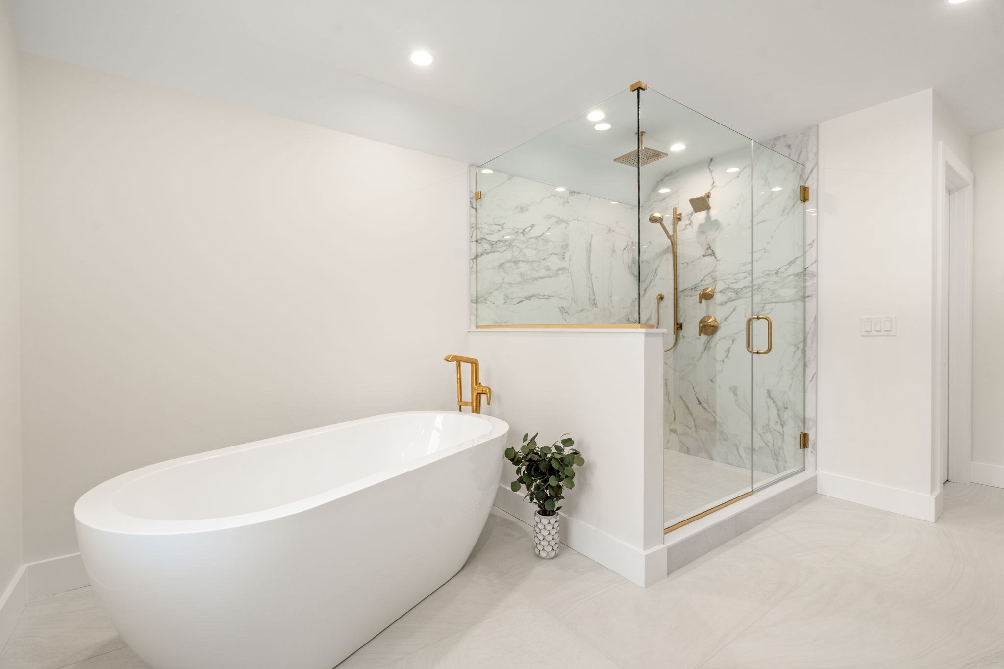 Modern bathroom with a freestanding soaking tub and marble shower with gold fixtures.