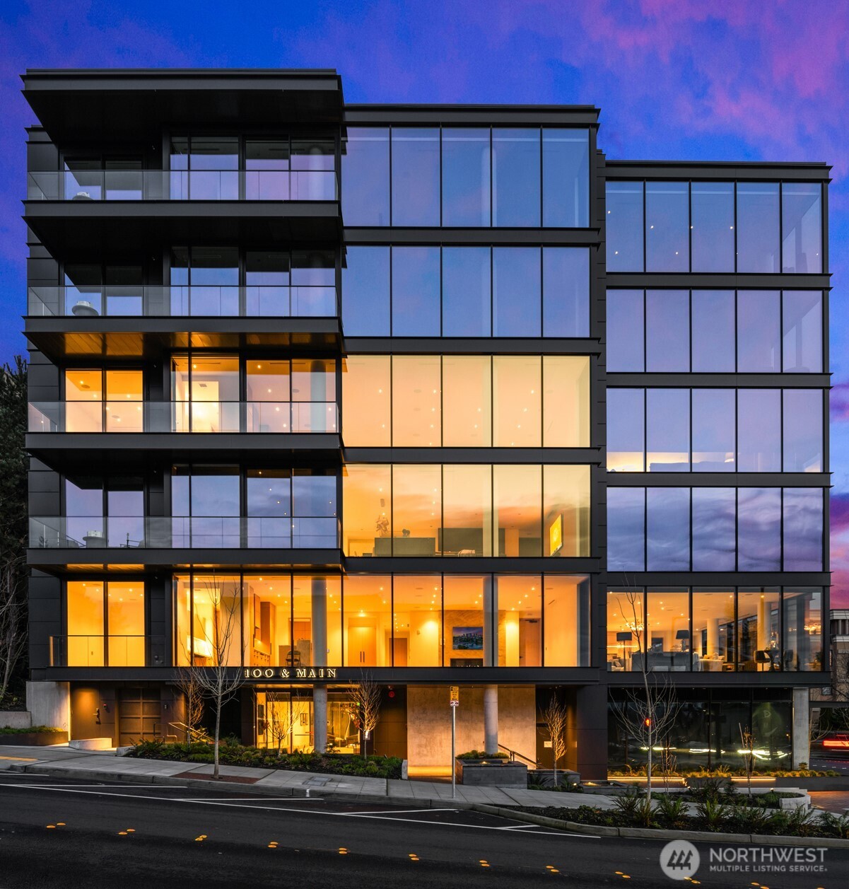 Modern glass condominium with illuminated interiors and balconies at dusk.