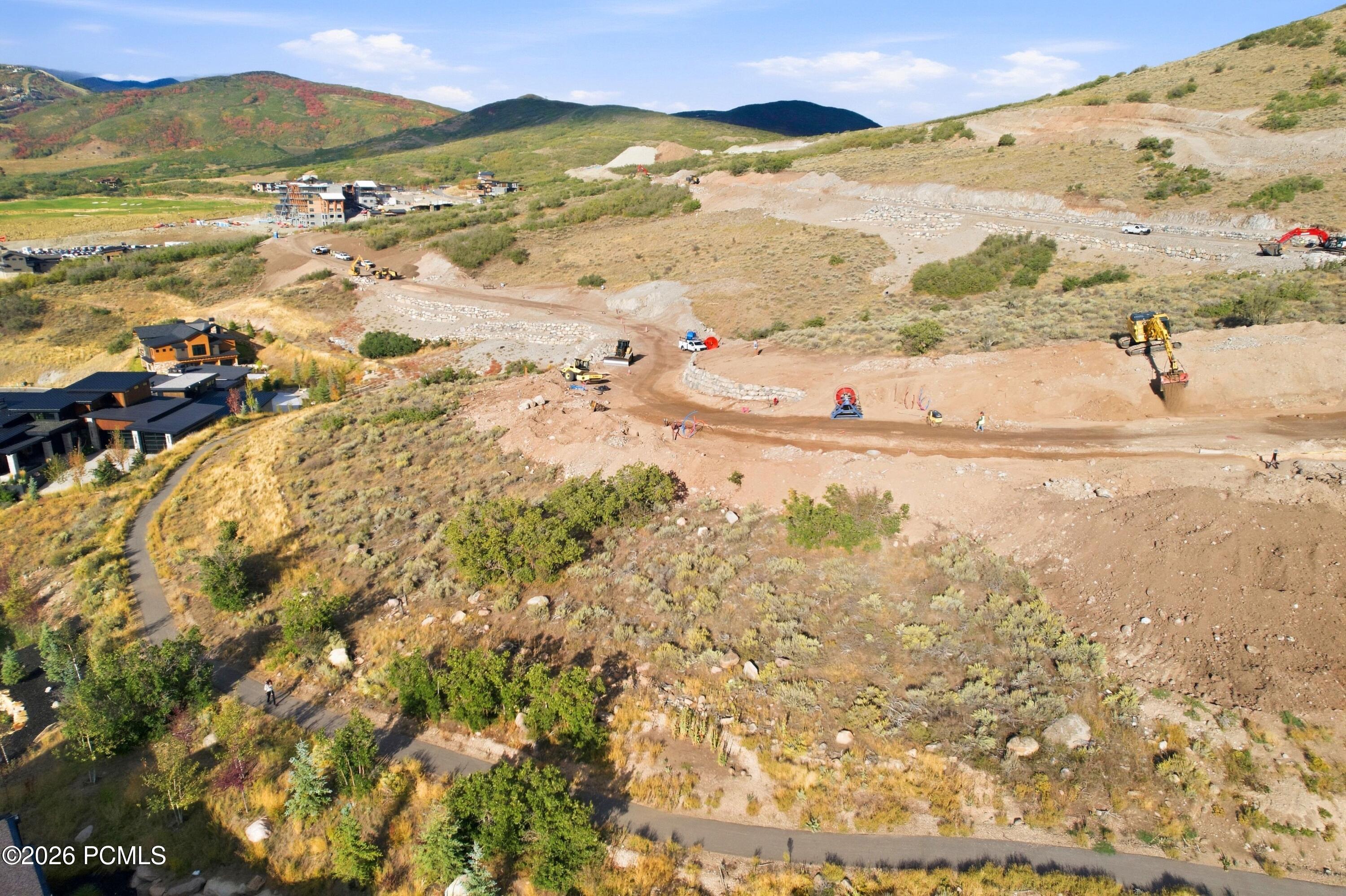 Aerial view of a hillside development under construction, with graded roads, construction equipment, and mountain ridges.
