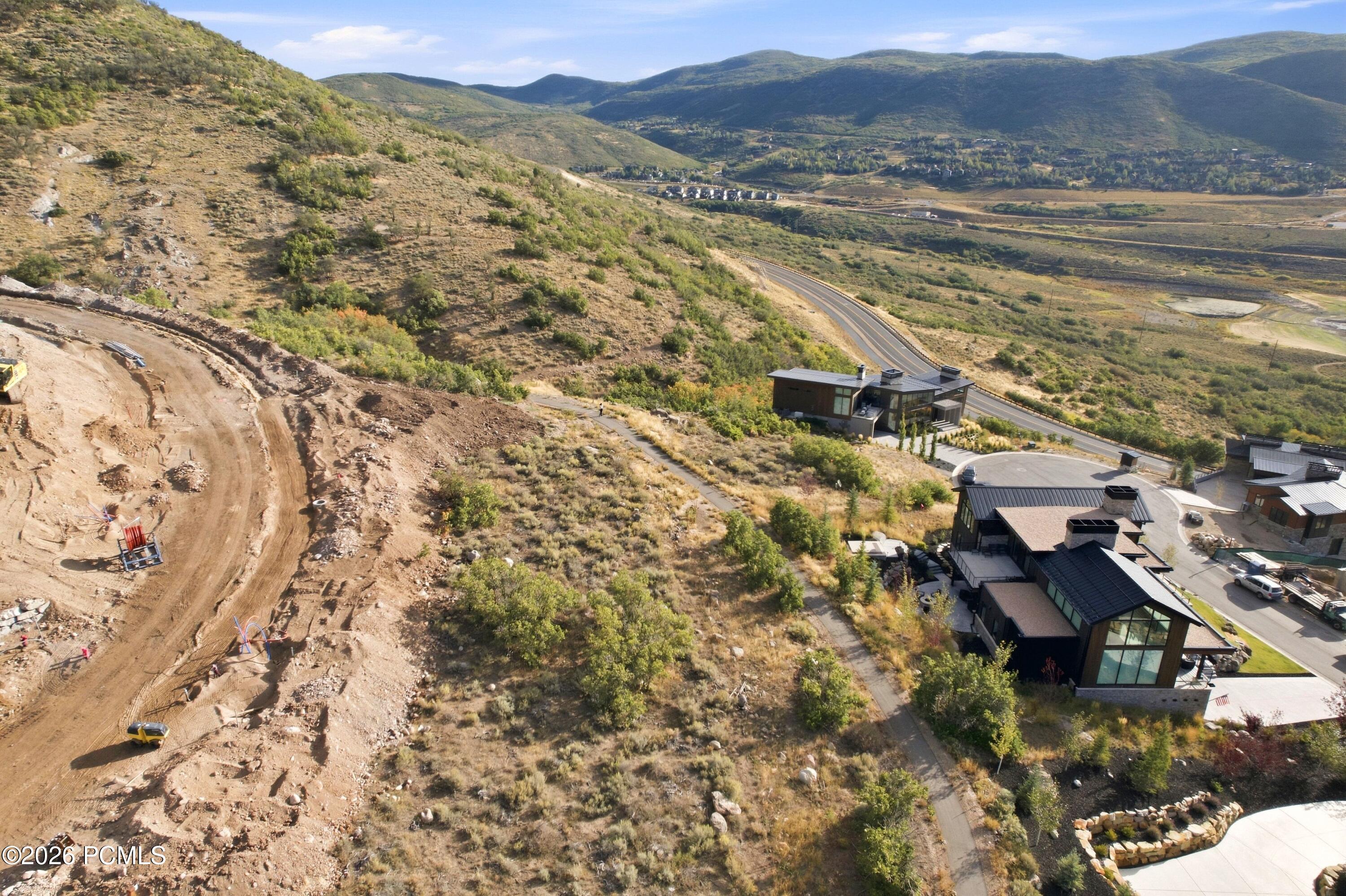 Aerial view of an excavated construction site beside modern homes, with mountain hills in the distance.