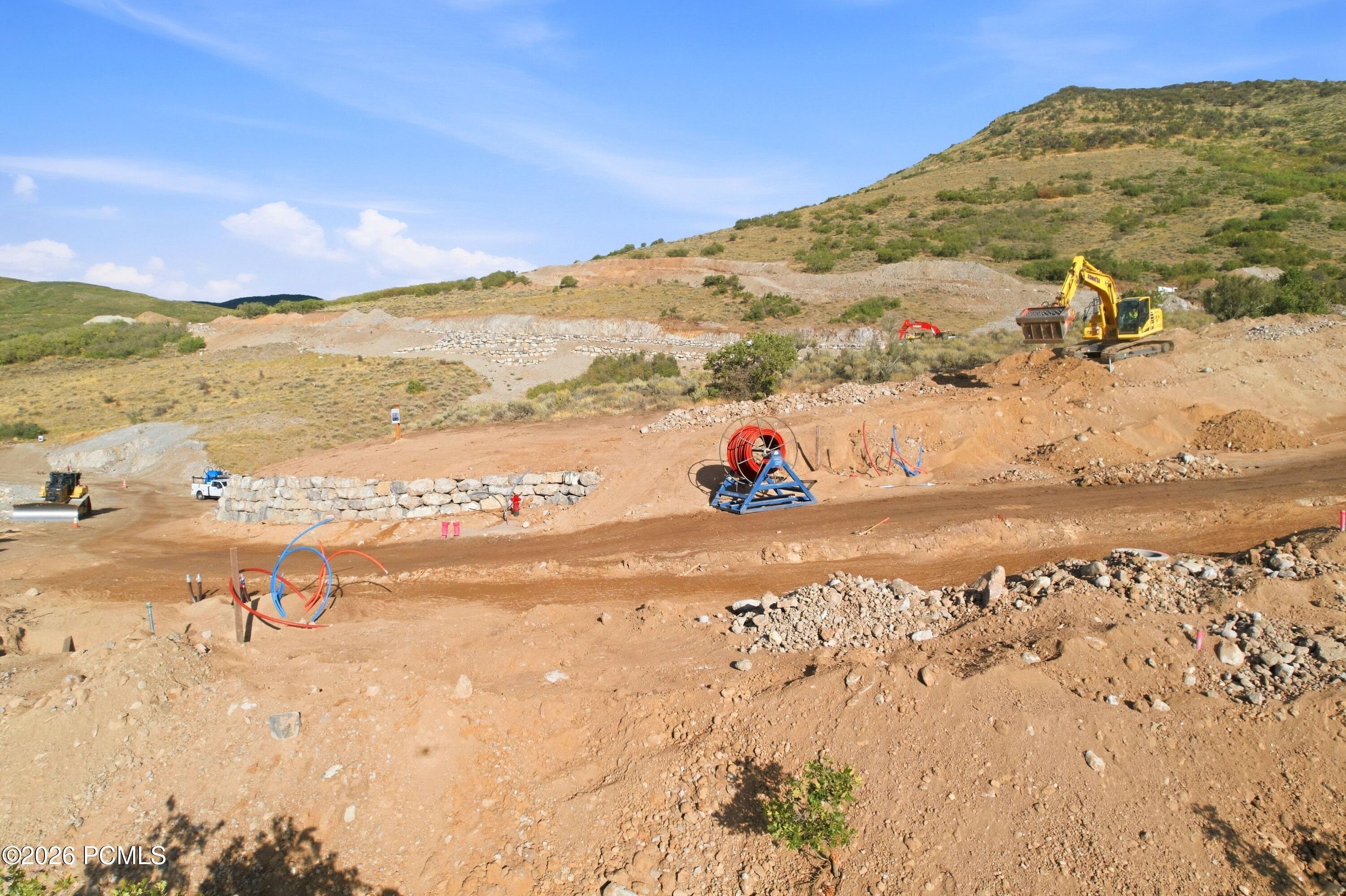 Hillside construction site with excavators, stone retaining walls, and exposed utility conduits.