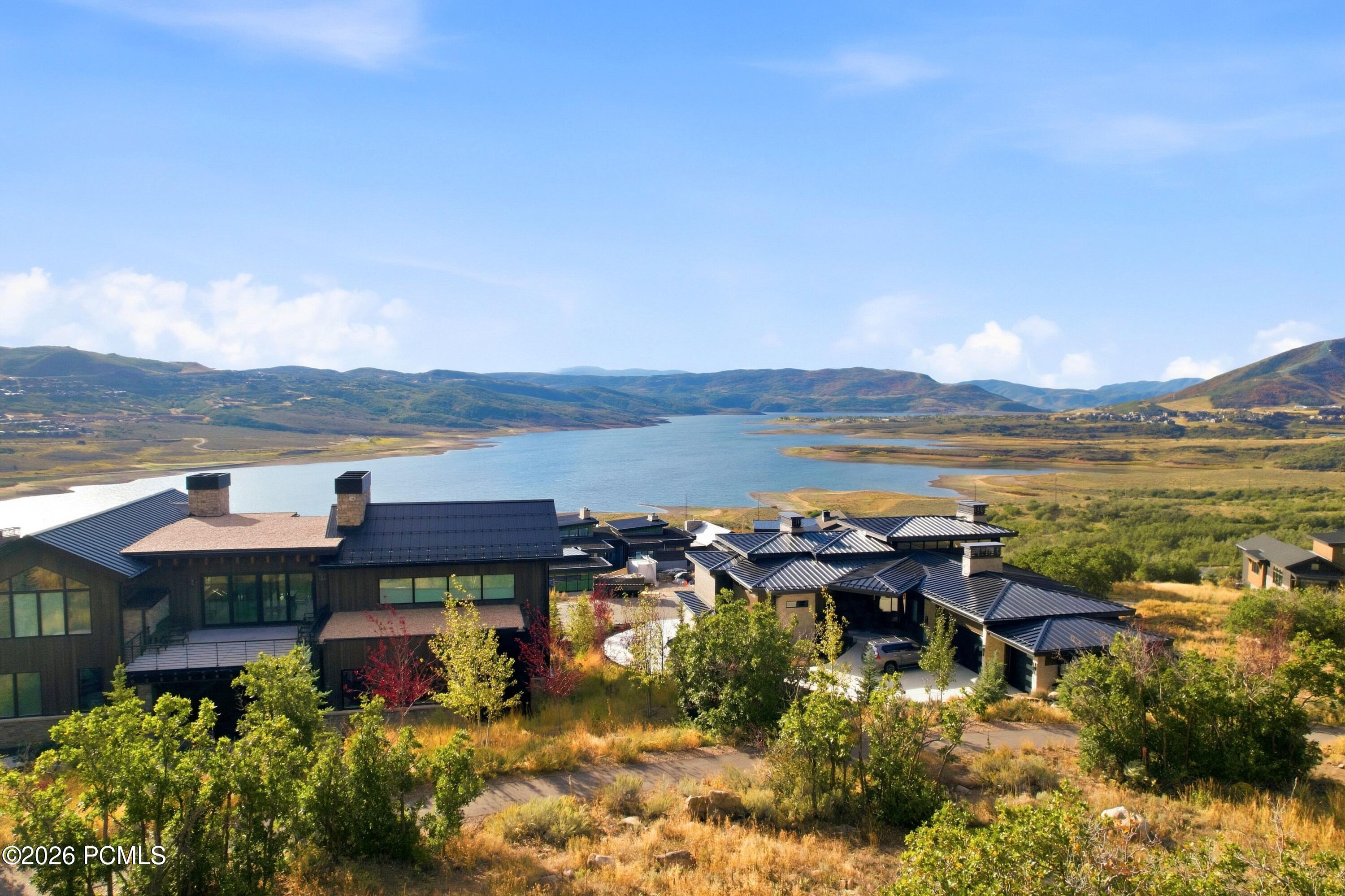 Modern mountain homes overlook a lake, with autumn hills and mountains beyond.