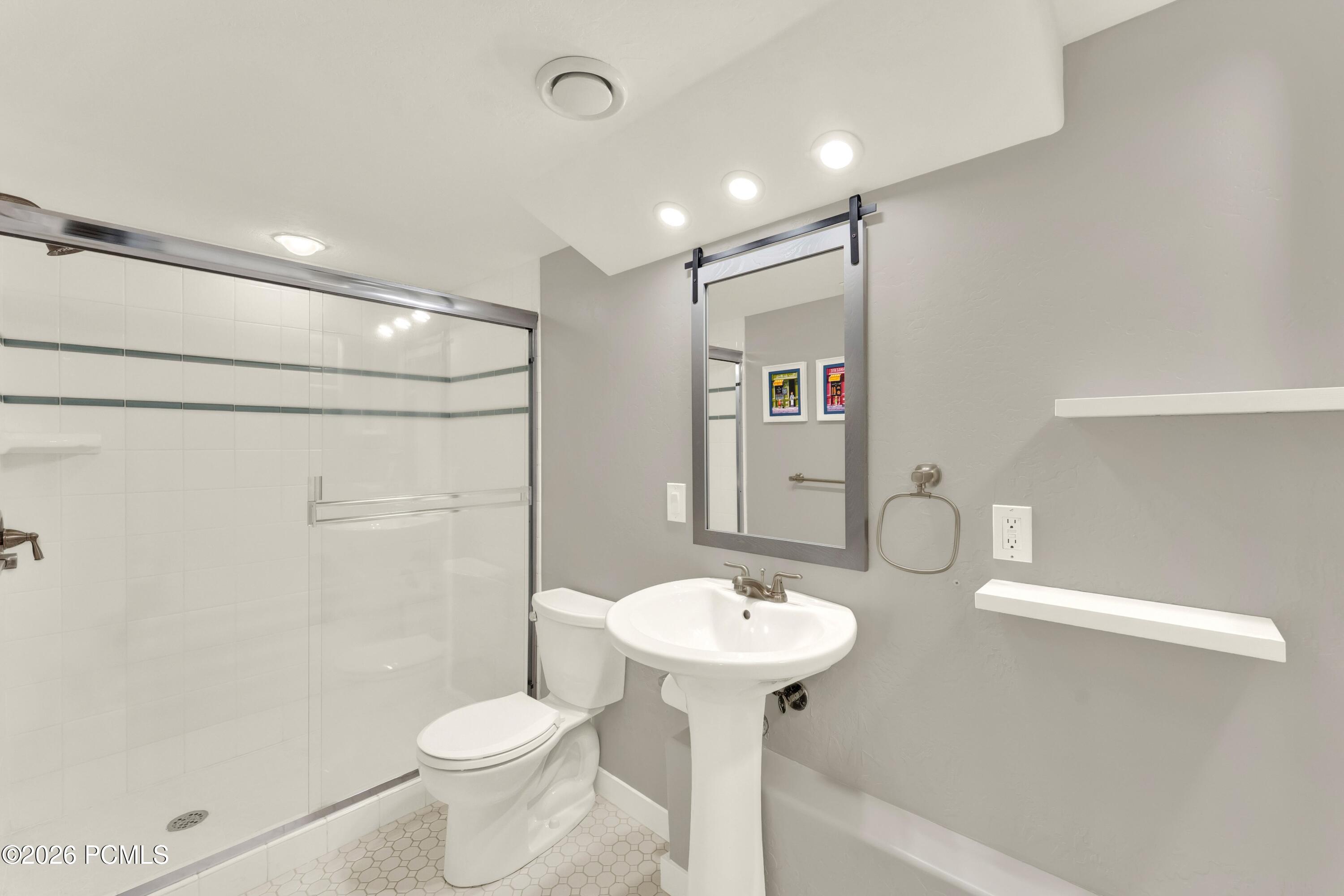 Bathroom with a glass shower, pedestal sink, and floating shelves.