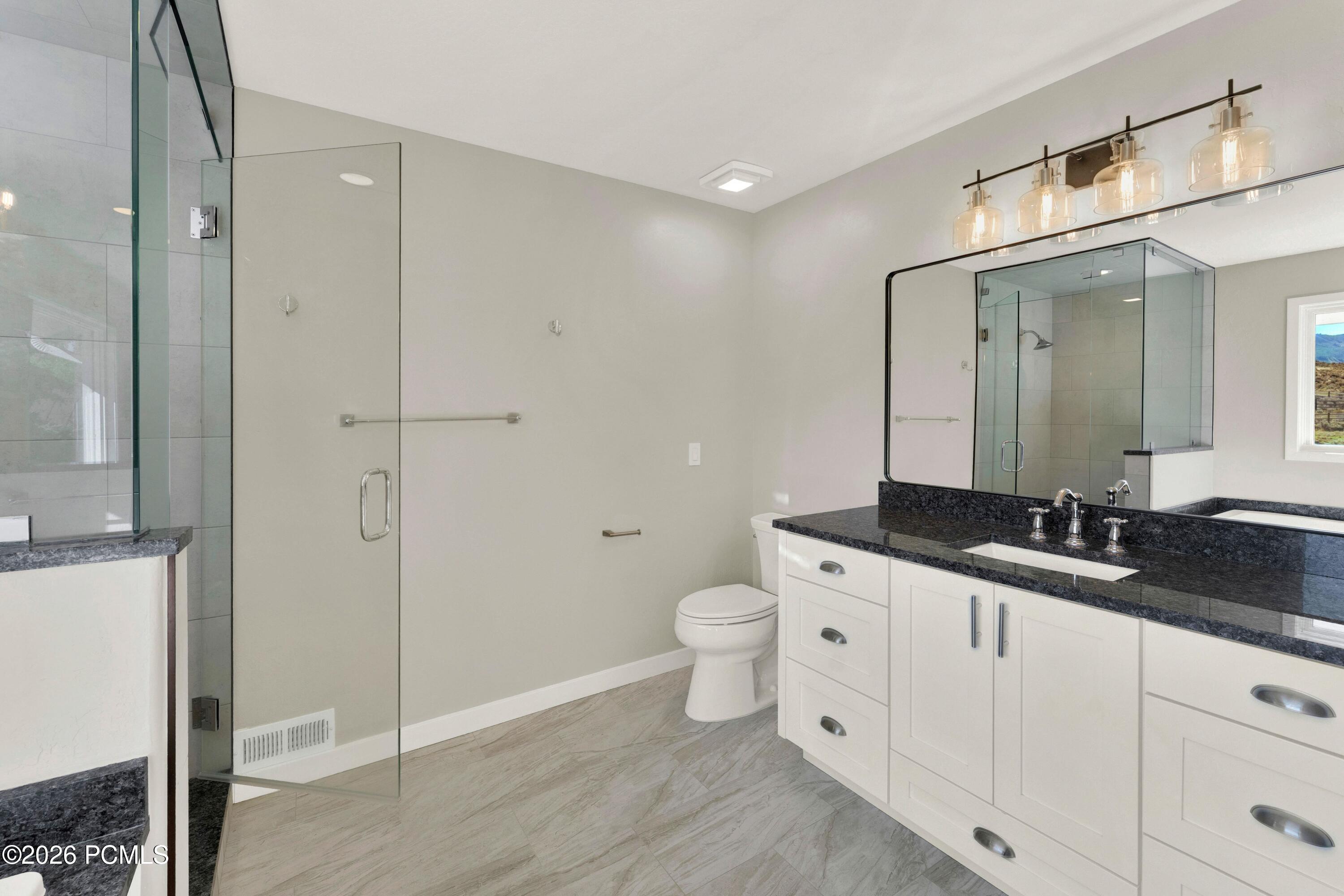 Modern bathroom with a glass shower and white vanity topped with dark granite.