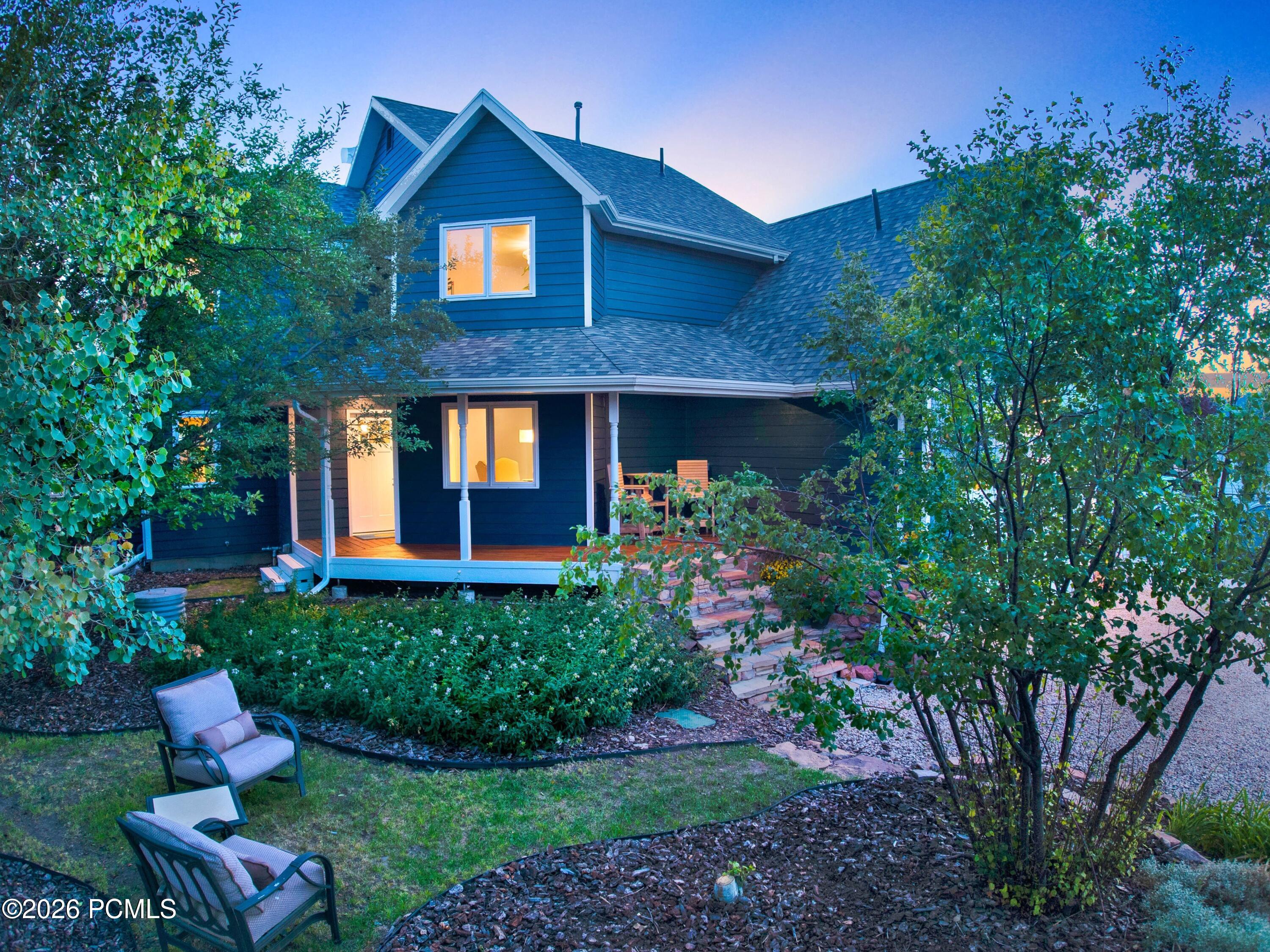 Dark blue two-story house with a covered porch and garden seating, warmly lit at dusk.