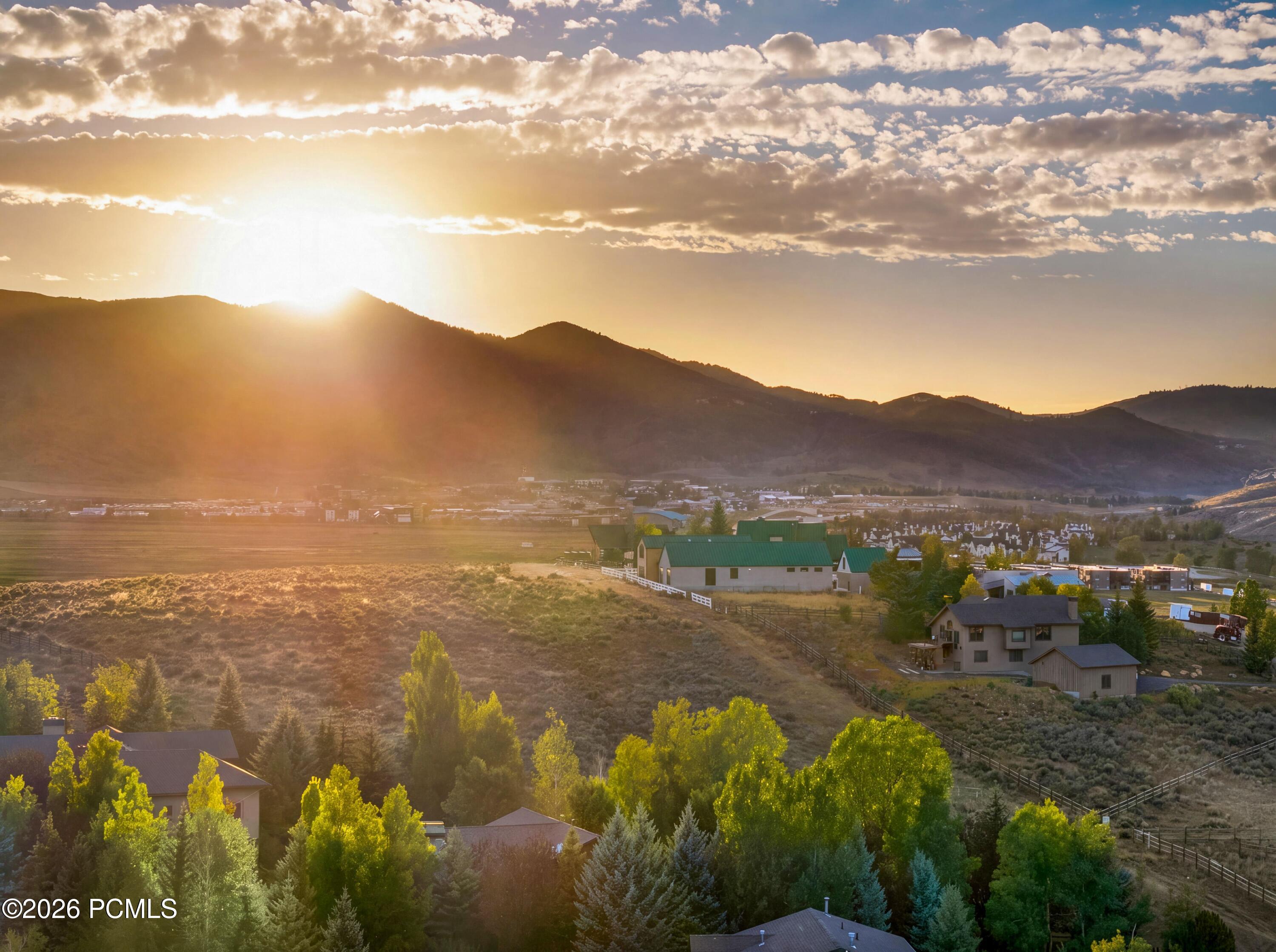 Mountain valley homes and open land beneath sunset-lit clouds and ridgelines.